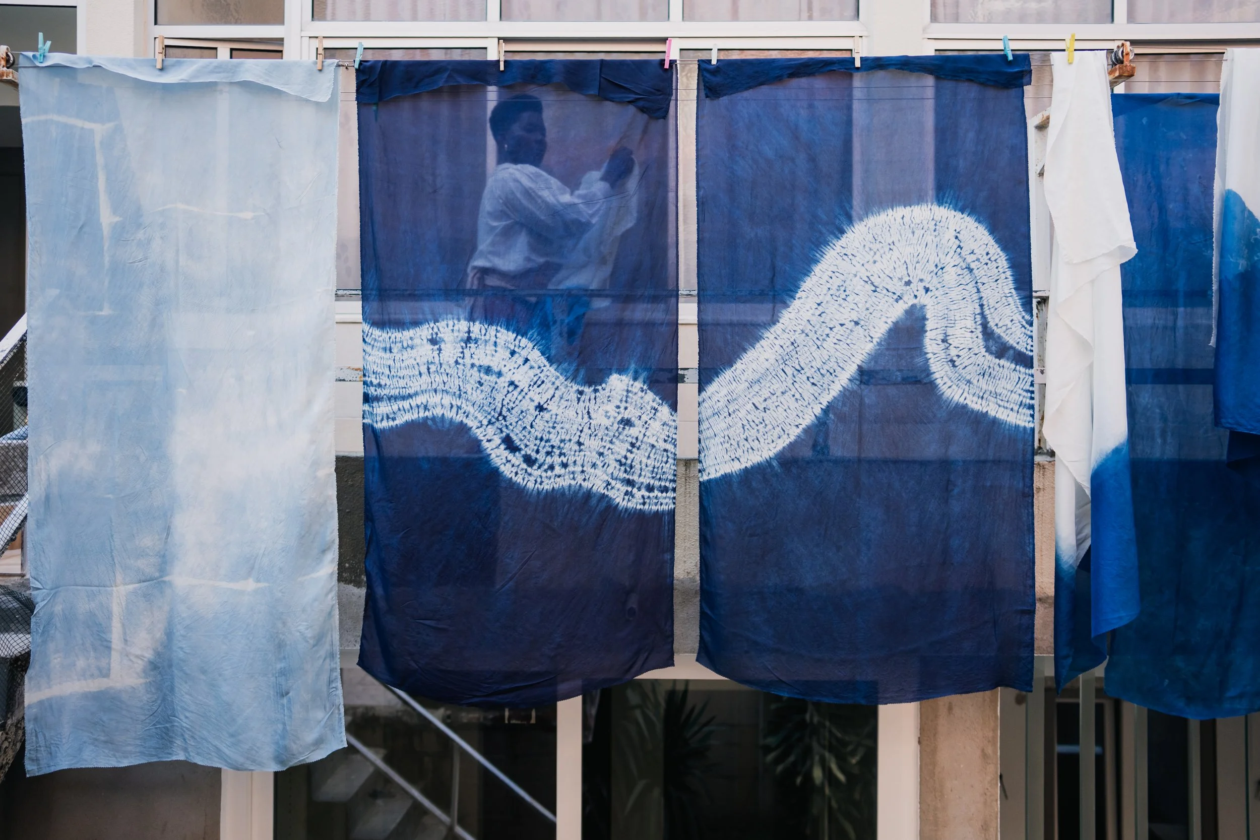 Clothes hanging on a line to dry, including a dark blue piece with white design resembling an arrow or snake, and other lighter pieces of fabric.