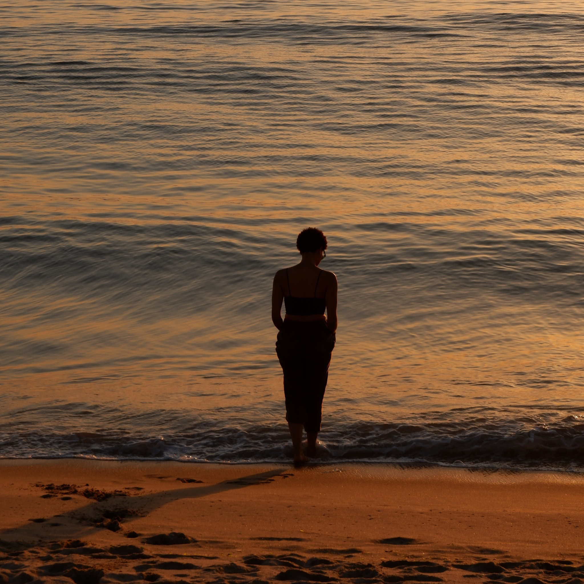 Silhouette of a woman standing on the beach at sunset, facing the water.