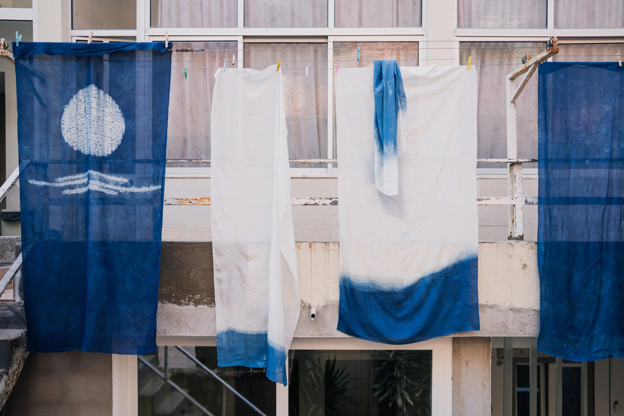 Clothes and fabric hanging on a clothesline outside an apartment building.