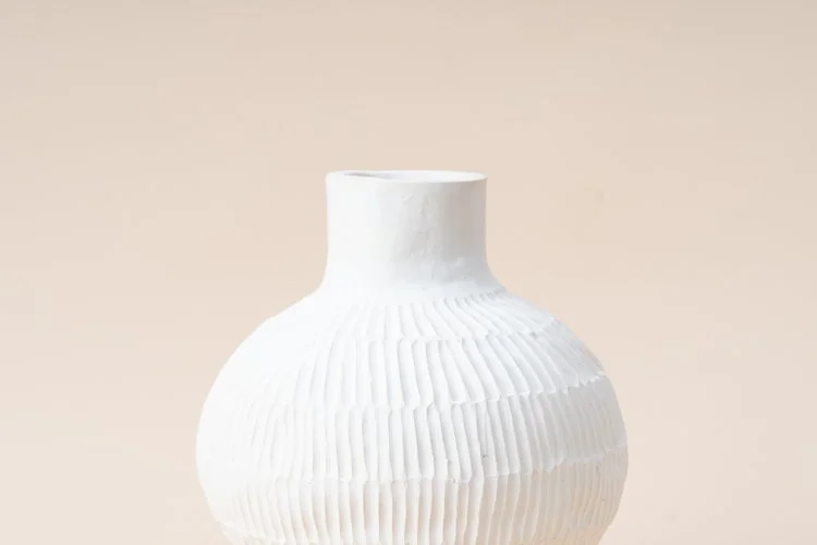 A white, textured ceramic vase with a narrow opening and ridged pattern, placed against a plain background.