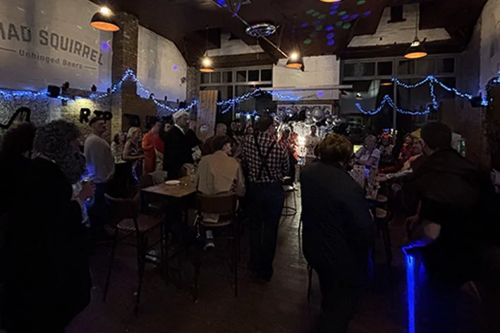 People socializing and drinking at the bar which is decorated with string lights.