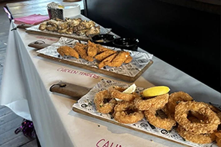 A table with various fried seafood dishes, including fried calamari and breaded fish, garnished with lemon wedges, at a restaurant or buffet.