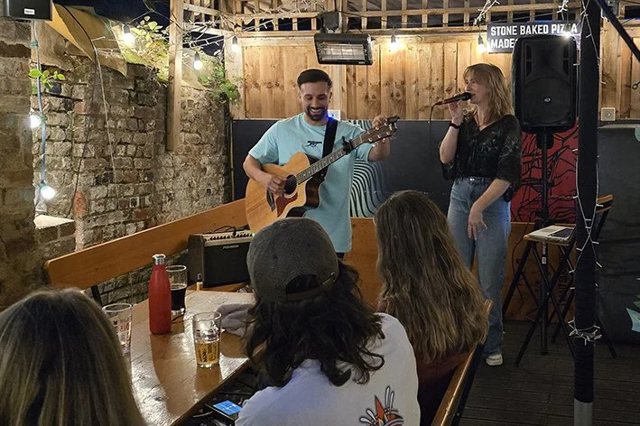 A man playing acoustic guitar and a woman singing into a microphone 