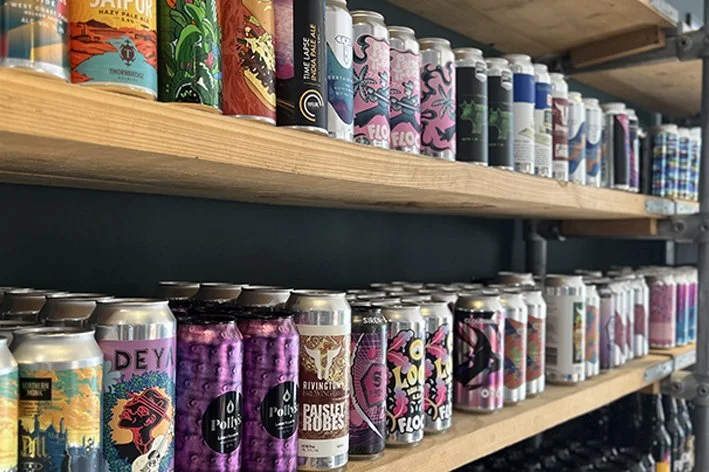 Shelves stocked with various colorful cans of craft beer on a wooden shelf in a store.