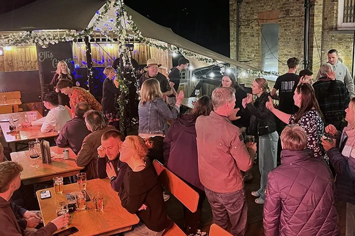 People gathered at an outdoor party dancing, with some sitting at tables and others standing and talking.