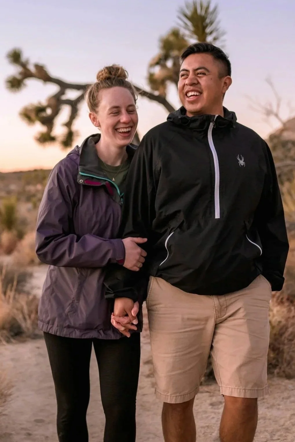 couple holding hands laughing while walking on a trail in the desert