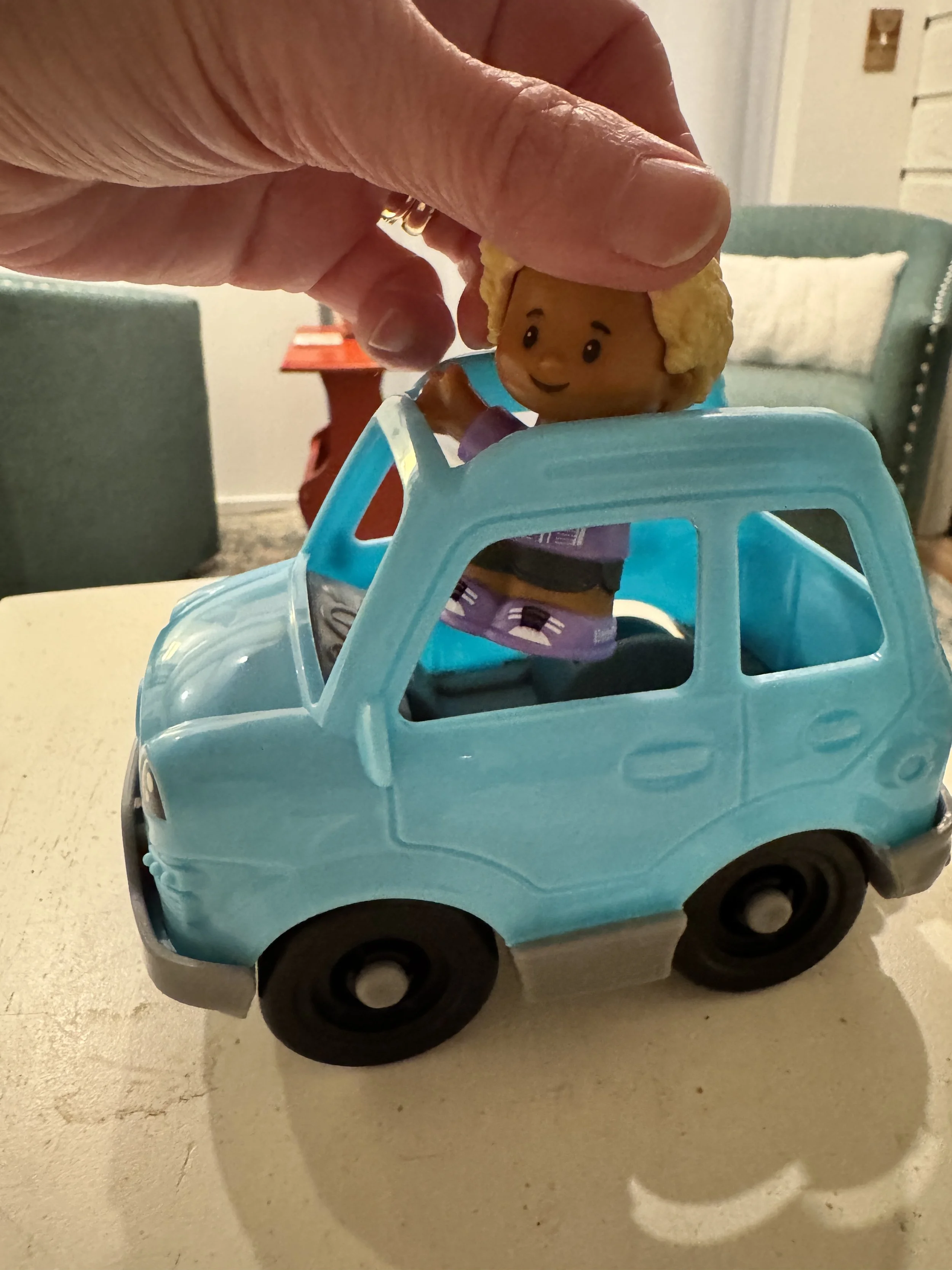 fisher price toy boy in a soccer jersey getting into a blue toy car.