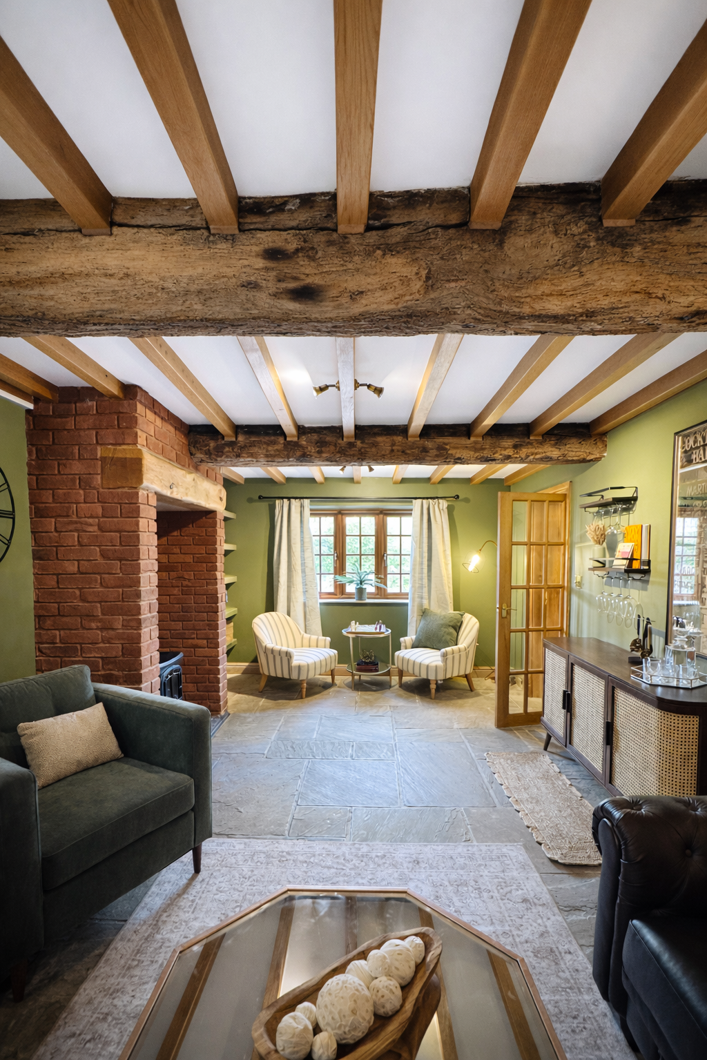 A warm, inviting living space defined by exposed timber beams, textured brickwork, and rich green walls. Layered with natural materials and soft upholstery, the room balances rustic character with refined detailing, featuring a cosy seating arrangeme