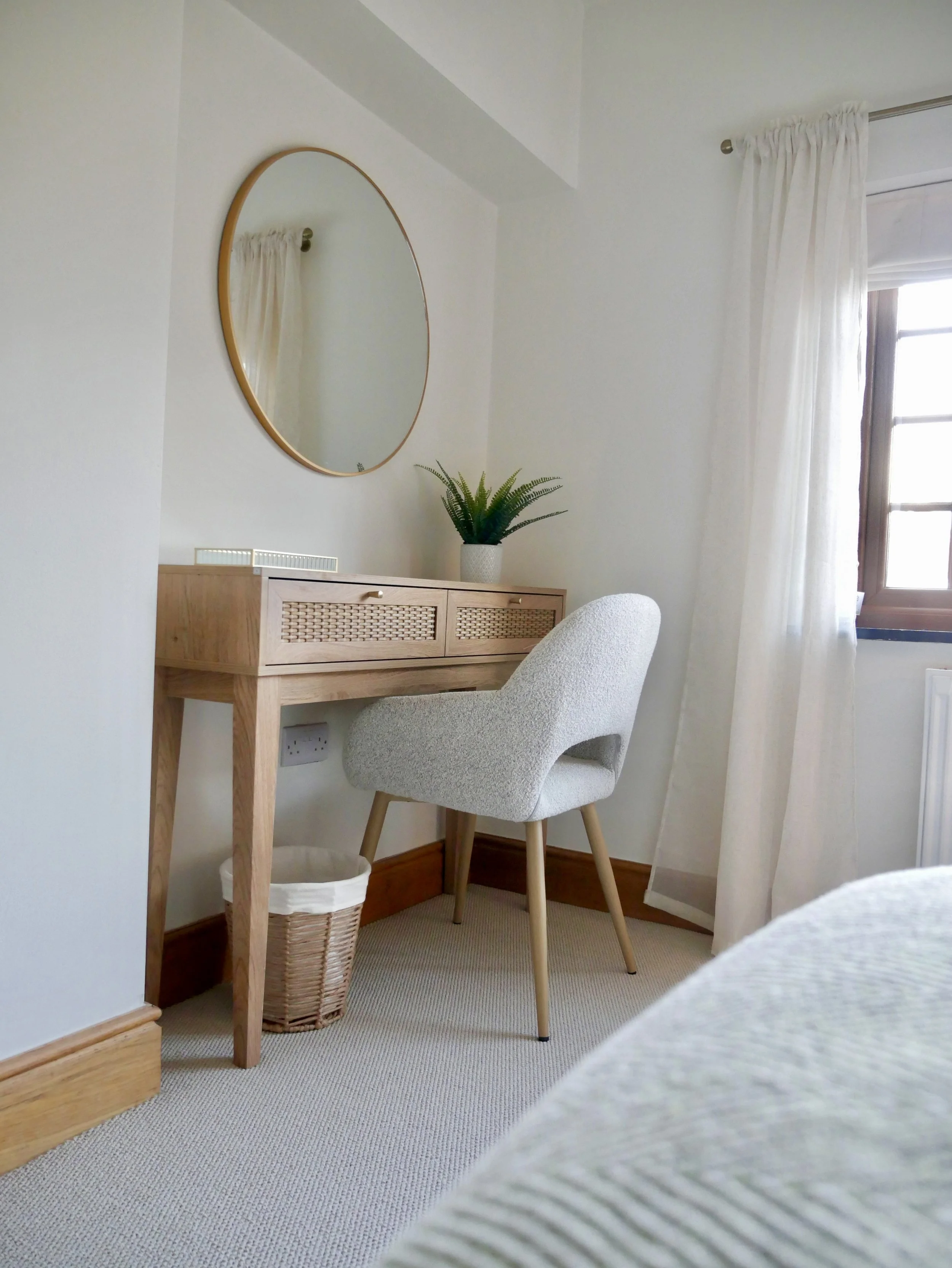 Elegant bedroom dressing table and workspace with round wall mirror, upholstered chair and woven storage basket in a modern Welsh holiday cottage. This bespoke interior design scheme blends soft neutrals, oak finishes and minimalist décor to create a