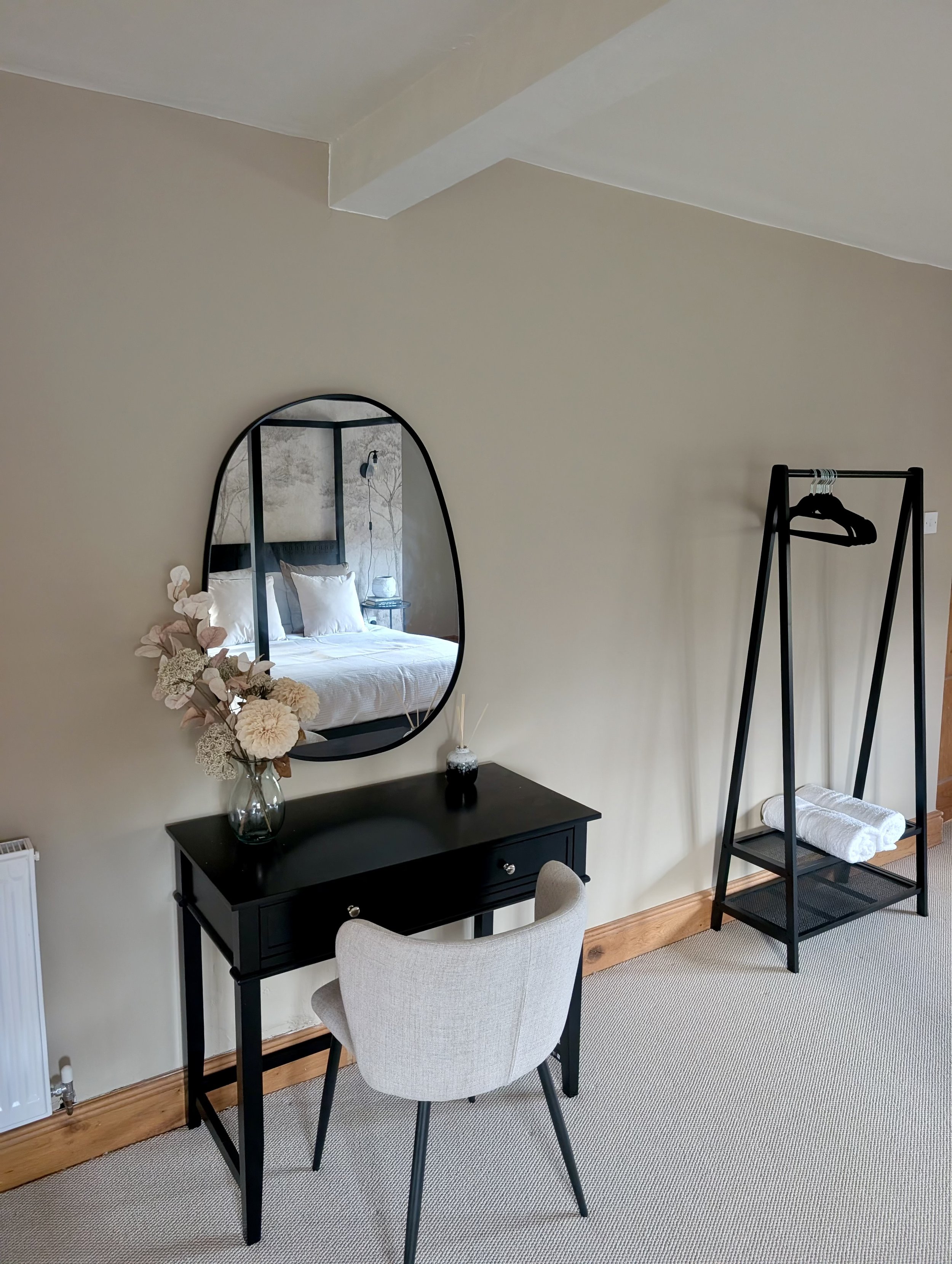 Styled bedroom corner with black console table, statement mirror and modern clothing rail in a beautifully designed UK holiday let. This thoughtfully curated interior combines practical storage with elegant, neutral décor to enhance light, space and 