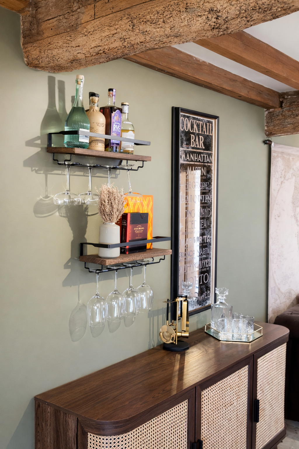 A warm, characterful corner styled as a compact home bar, set against soft sage-green walls and framed by rustic exposed timber beams overhead.

Two slim black metal and wood shelves are mounted on the wall, neatly arranged with an assortment of spir