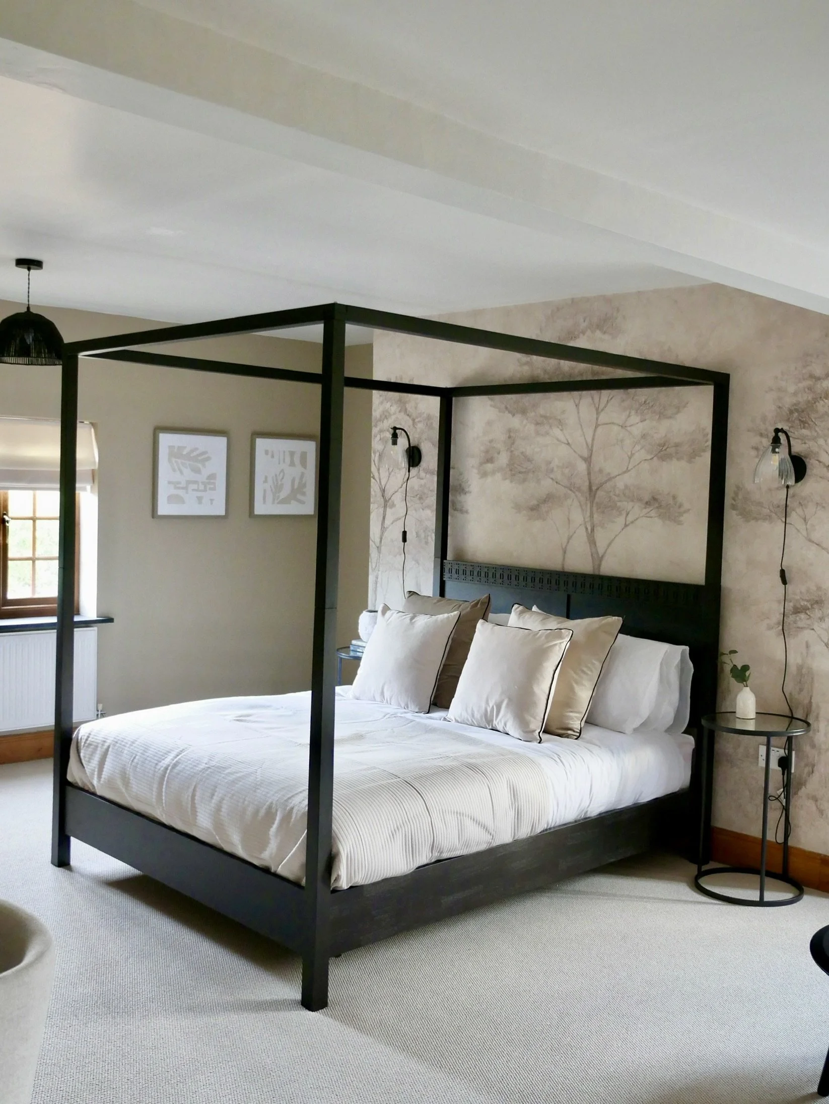 Luxury master bedroom with black four-poster bed, layered neutral bedding and feature botanical wallpaper in a Wales countryside holiday home. A boutique-style interior design scheme combining contemporary comfort with warm natural textures and soft,
