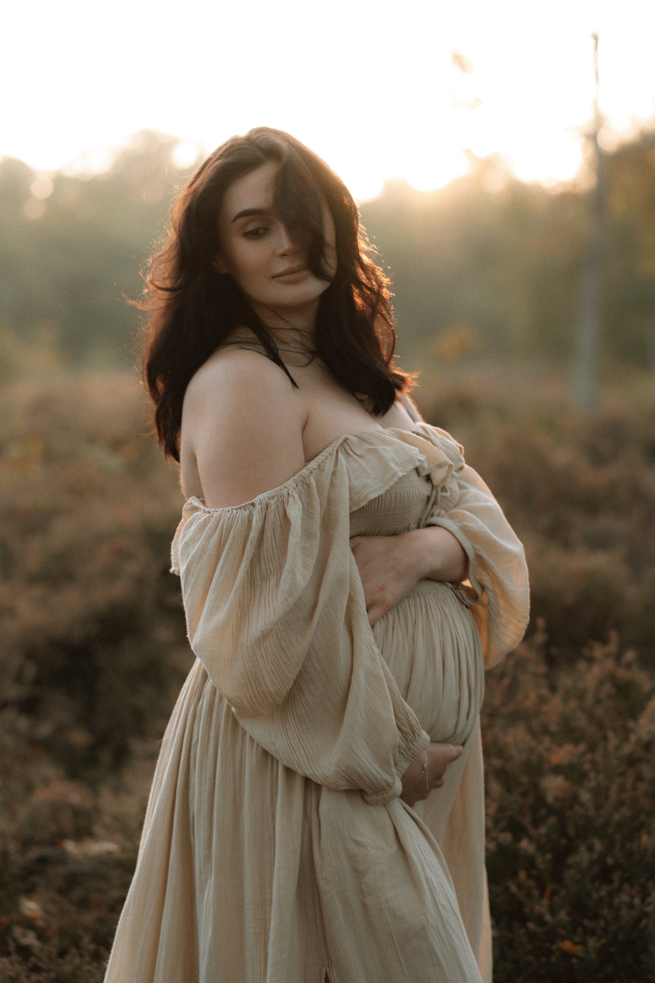 A pregnant woman cradling her bump at sunset during an outdoor maternity photography session in Oxfordshire