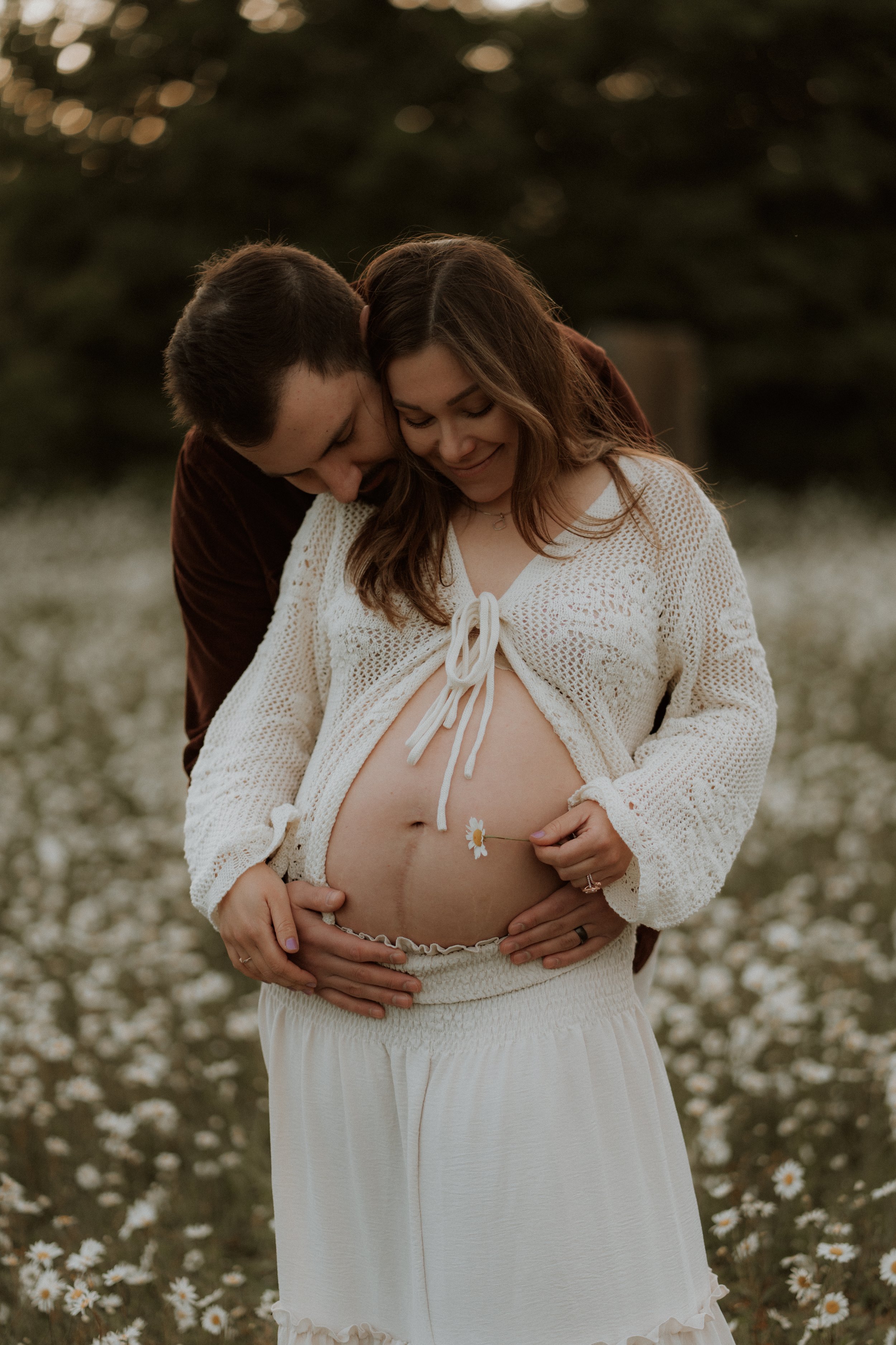 A couple embracing in a wildflower meadow, with the expectant mother cradling her baby bump during an outdoor maternity photography session in Oxfordshire.