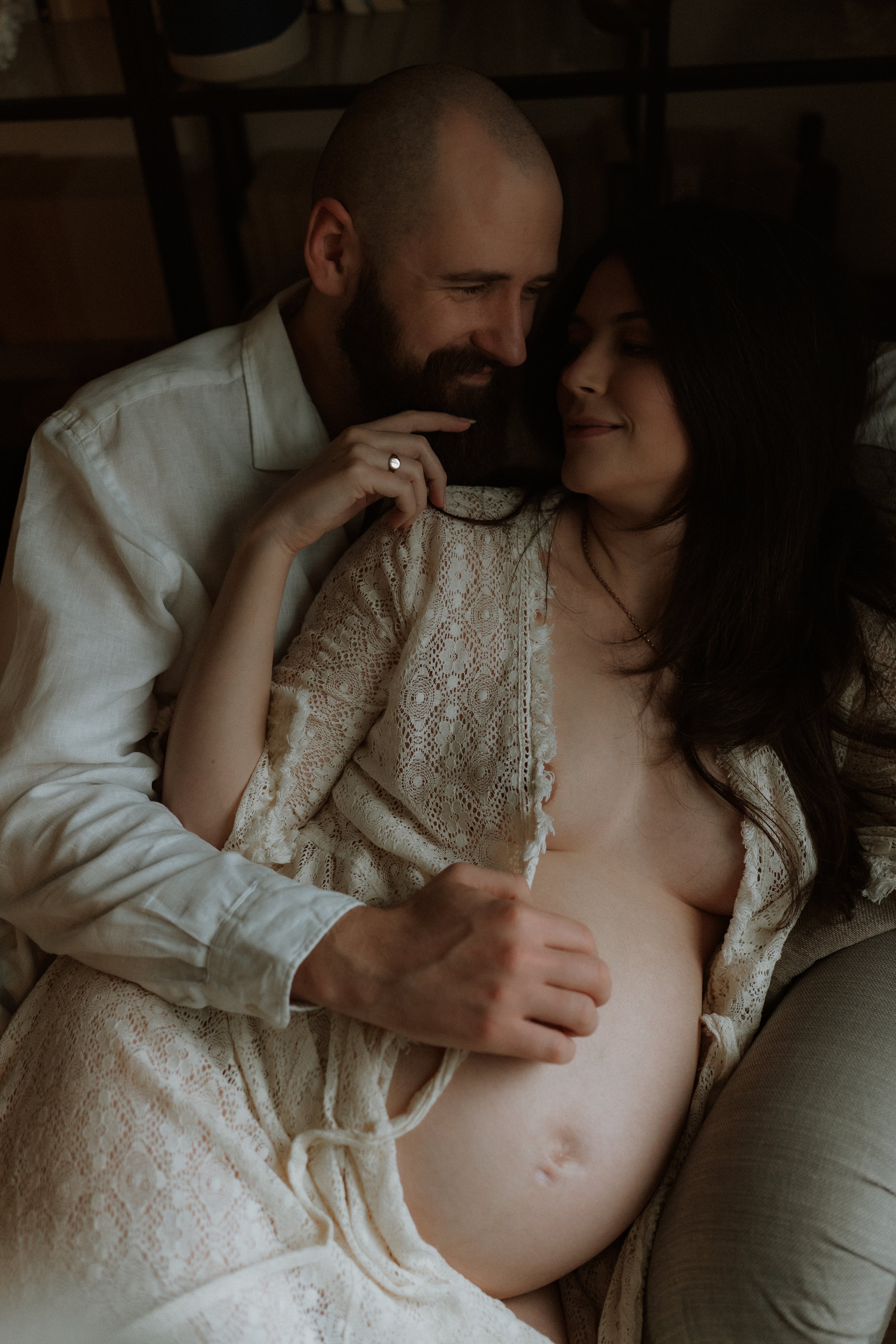 A pregnant woman embracing her partner during an intimate in-home maternity photography session in Oxfordshire, with his hand resting gently on her bump