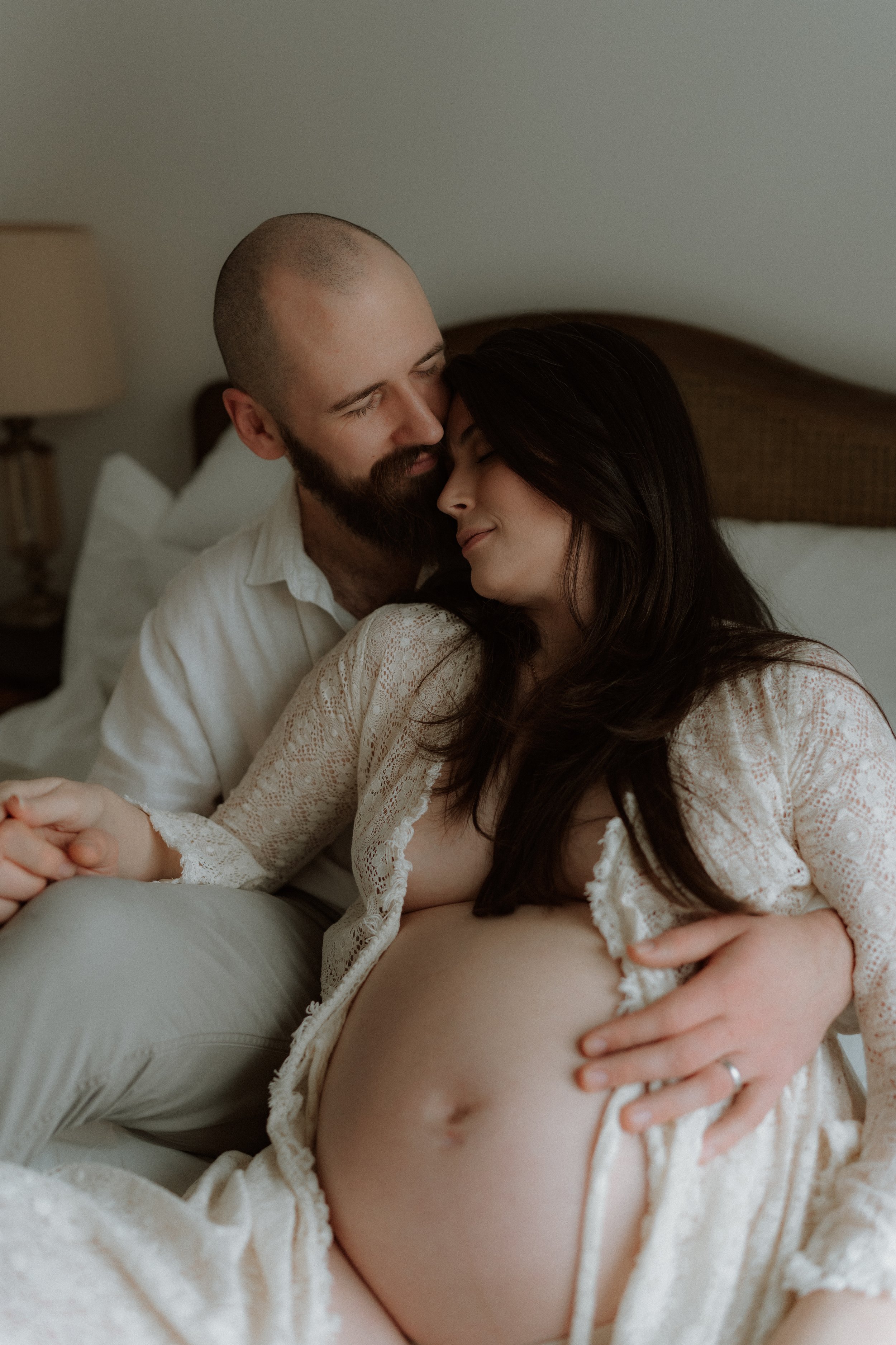 A pregnant woman cuddling with her partner during an in-home maternity photography session in Oxfordshire