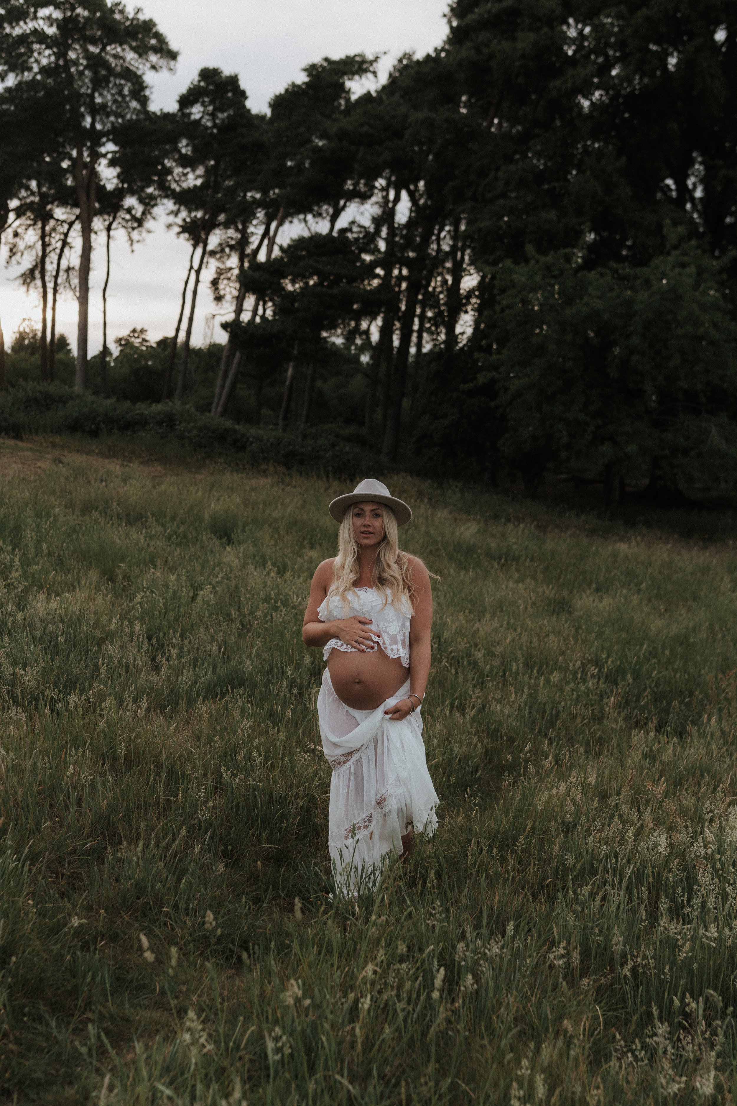 An expectant mother cradling her baby bump in a long grass meadow during a golden hour maternity photography session in Oxfordshire.