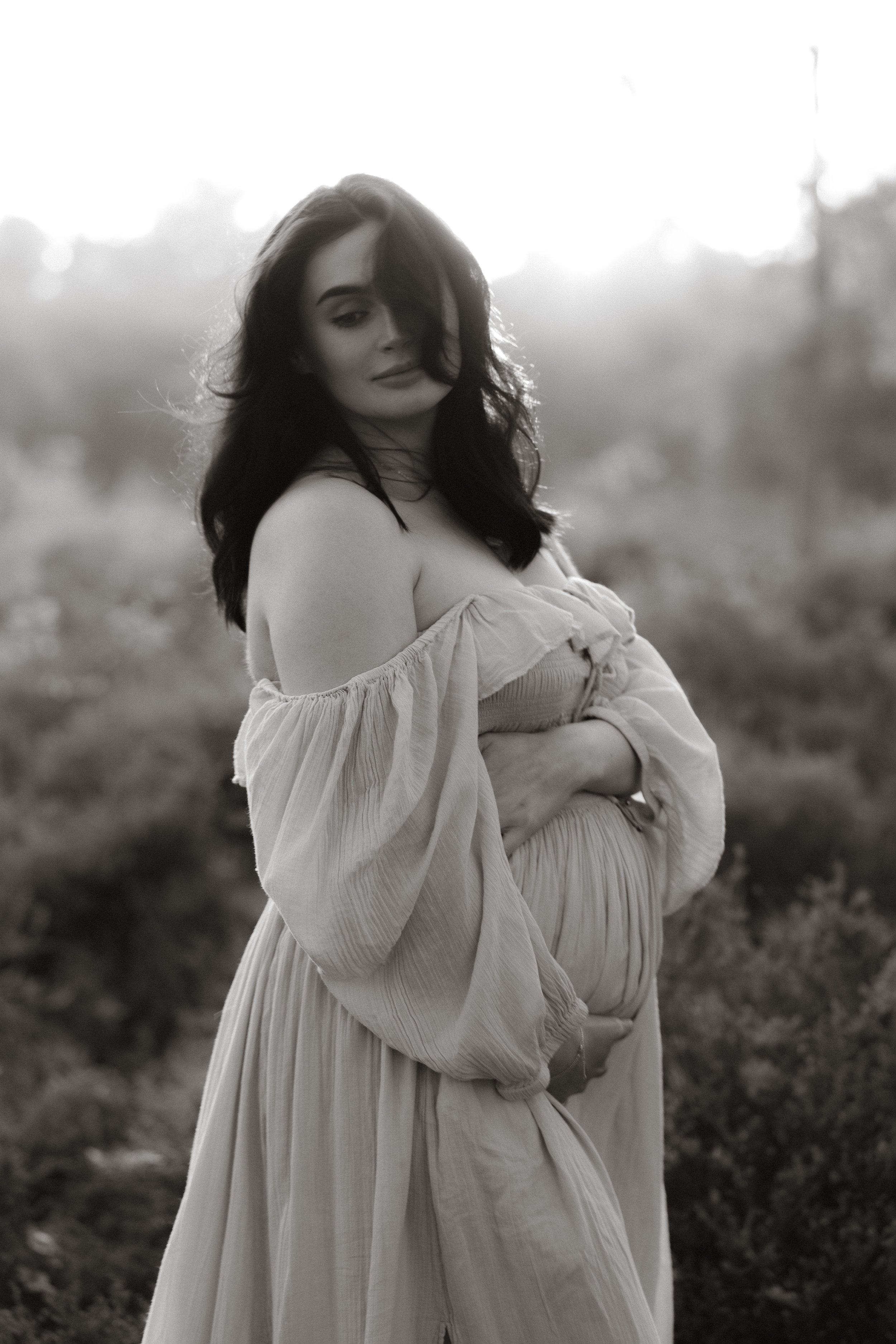 A pregnant woman cradling her bump at sunset during an outdoor maternity photography session near Oxford