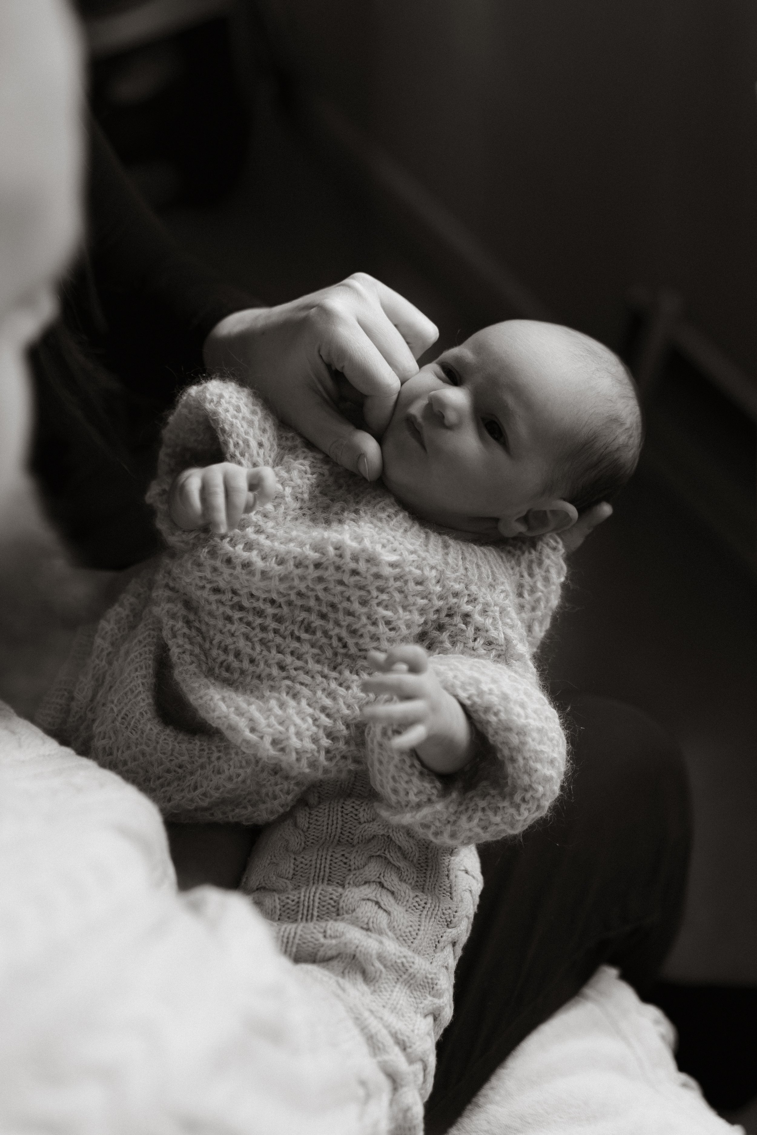 A newborn baby cuddled safely in a parent’s arms during an in-home newborn photography session in Oxfordshire, captured in soft natural light.