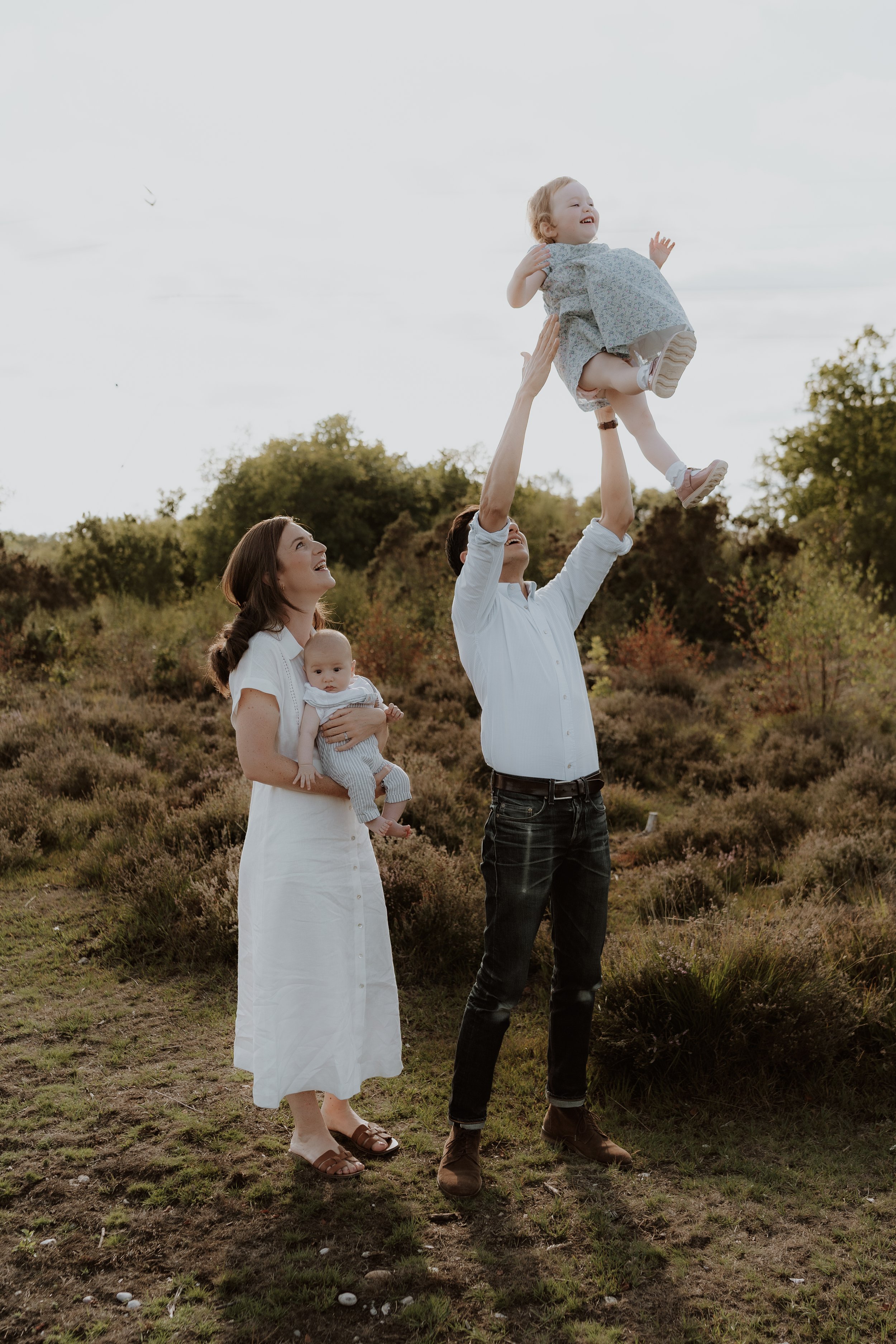 Parents lifting their toddler into the air during a relaxed outdoor family photography session in Oxfordshire
