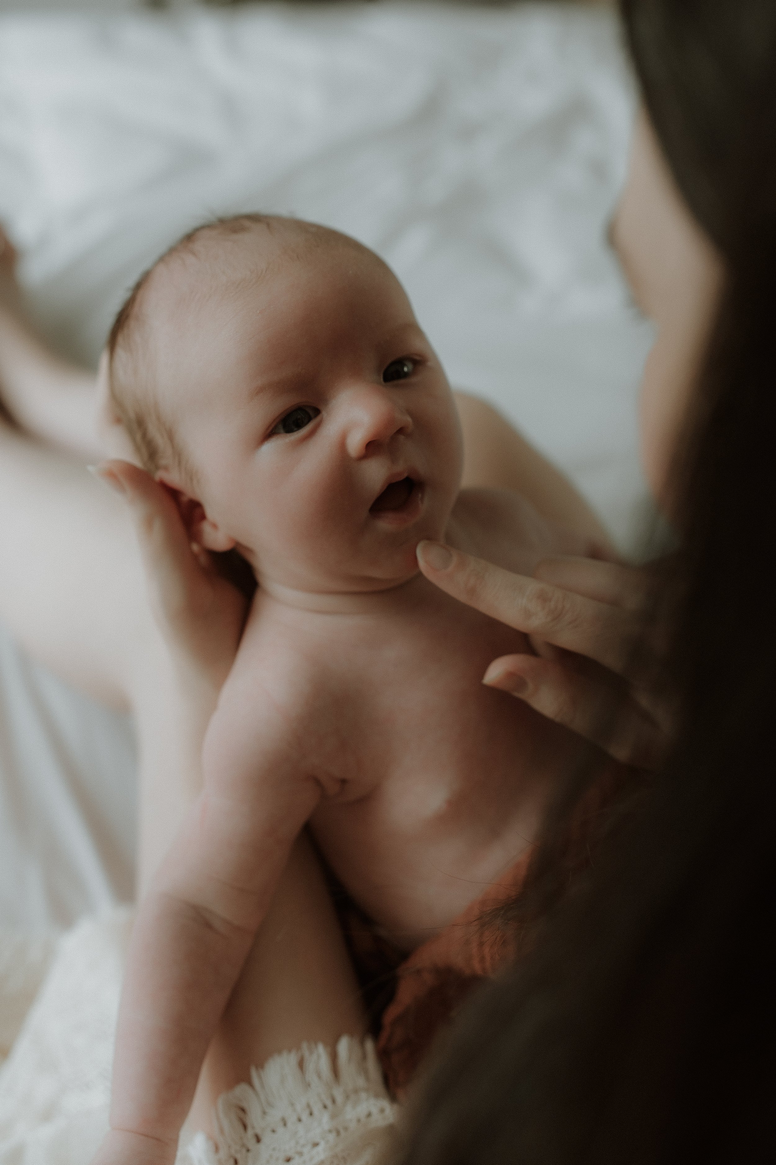 A new mum stroking her newborn baby's face during an in-home newborn photography session in Oxfordshire