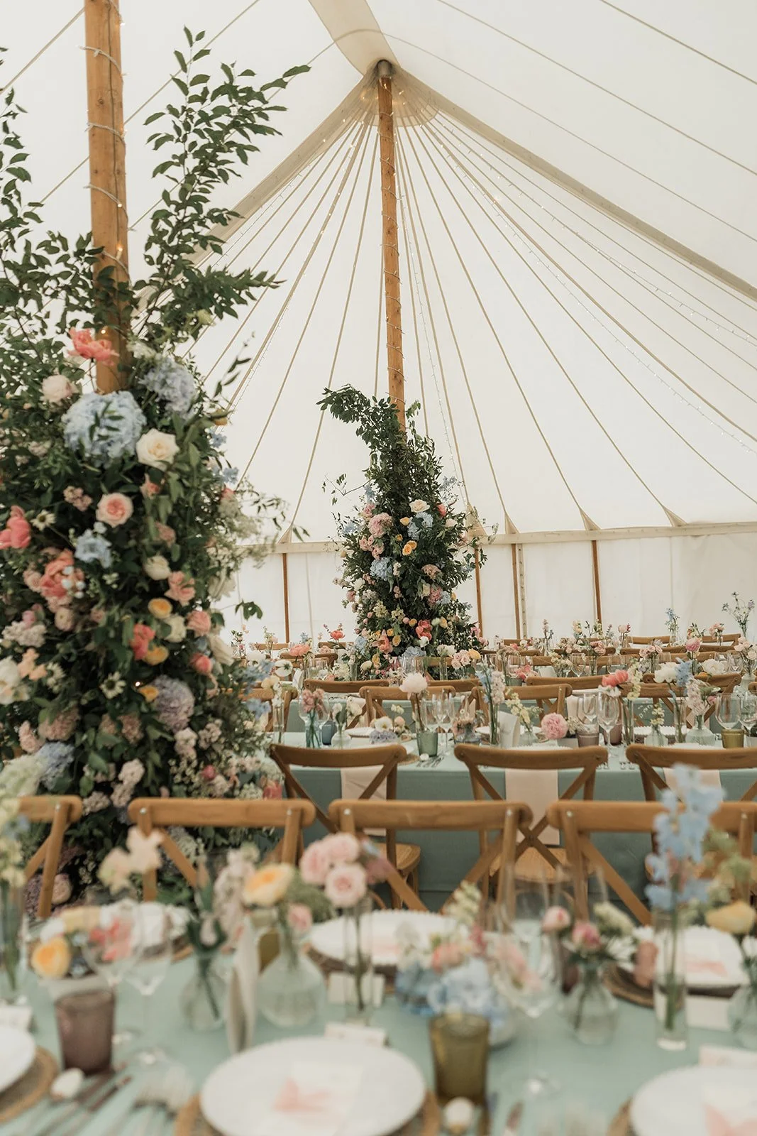 Luxury UK Wedding reception inside a sailcloth marquee decorated with pink, white, and blue flowers, with round tables set with floral centerpieces, glassware, and plates.
