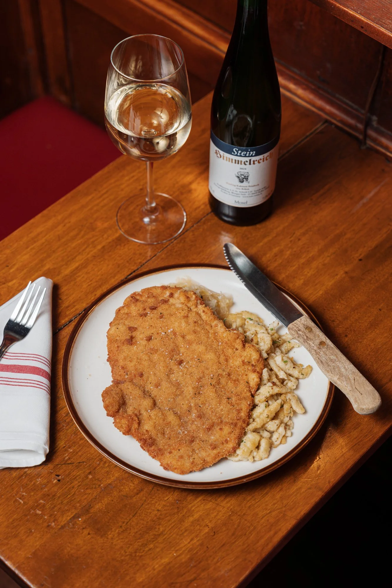 a Crispy Schnitzel served over Spätzle (German egg noodle), accompanied by a glass of white wine and a bottle of white wine. At The Student Prince in Springfield MA