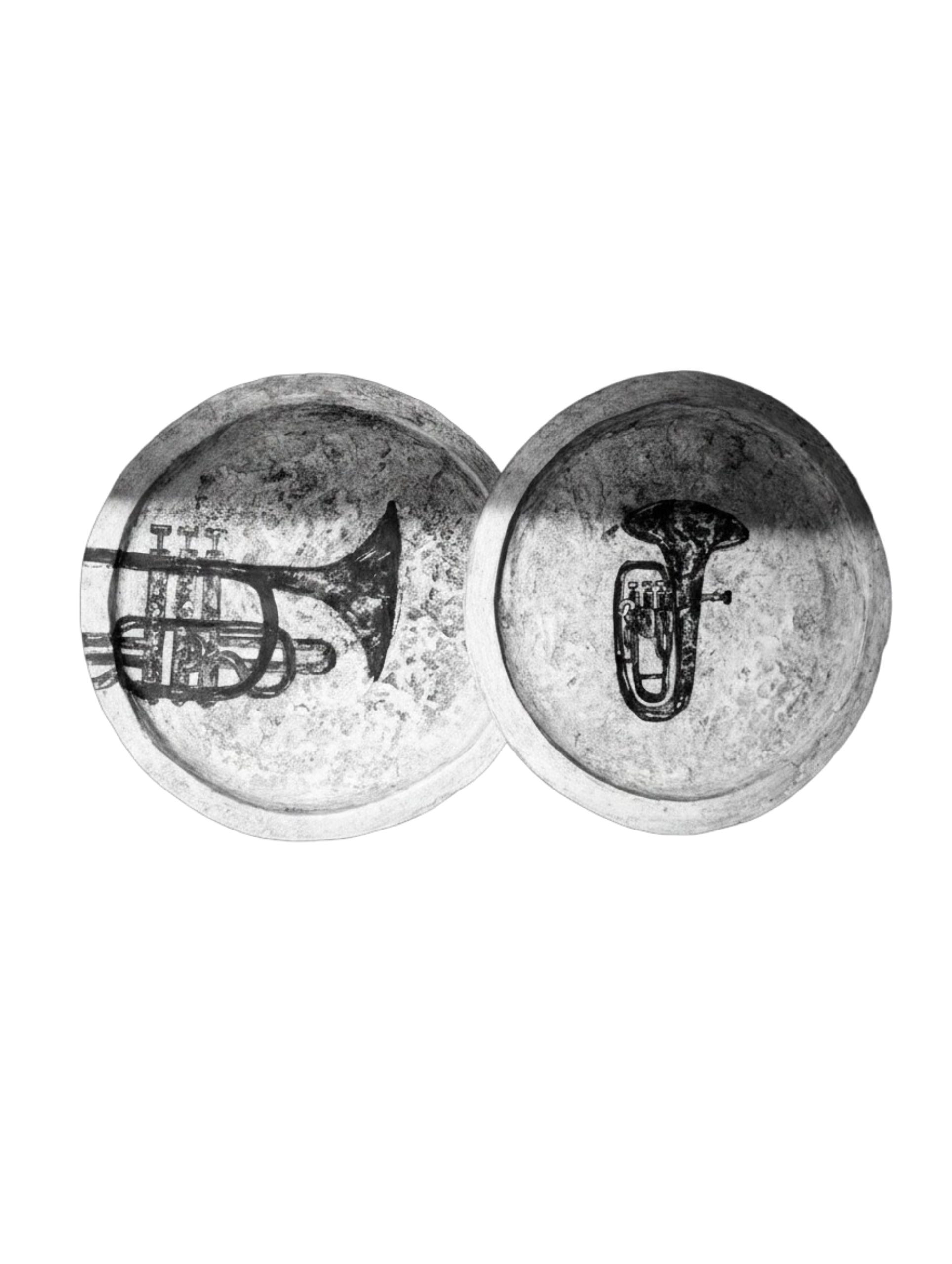 Two round metal objects with black illustrations of brass instruments on their surfaces, set against a dark background.