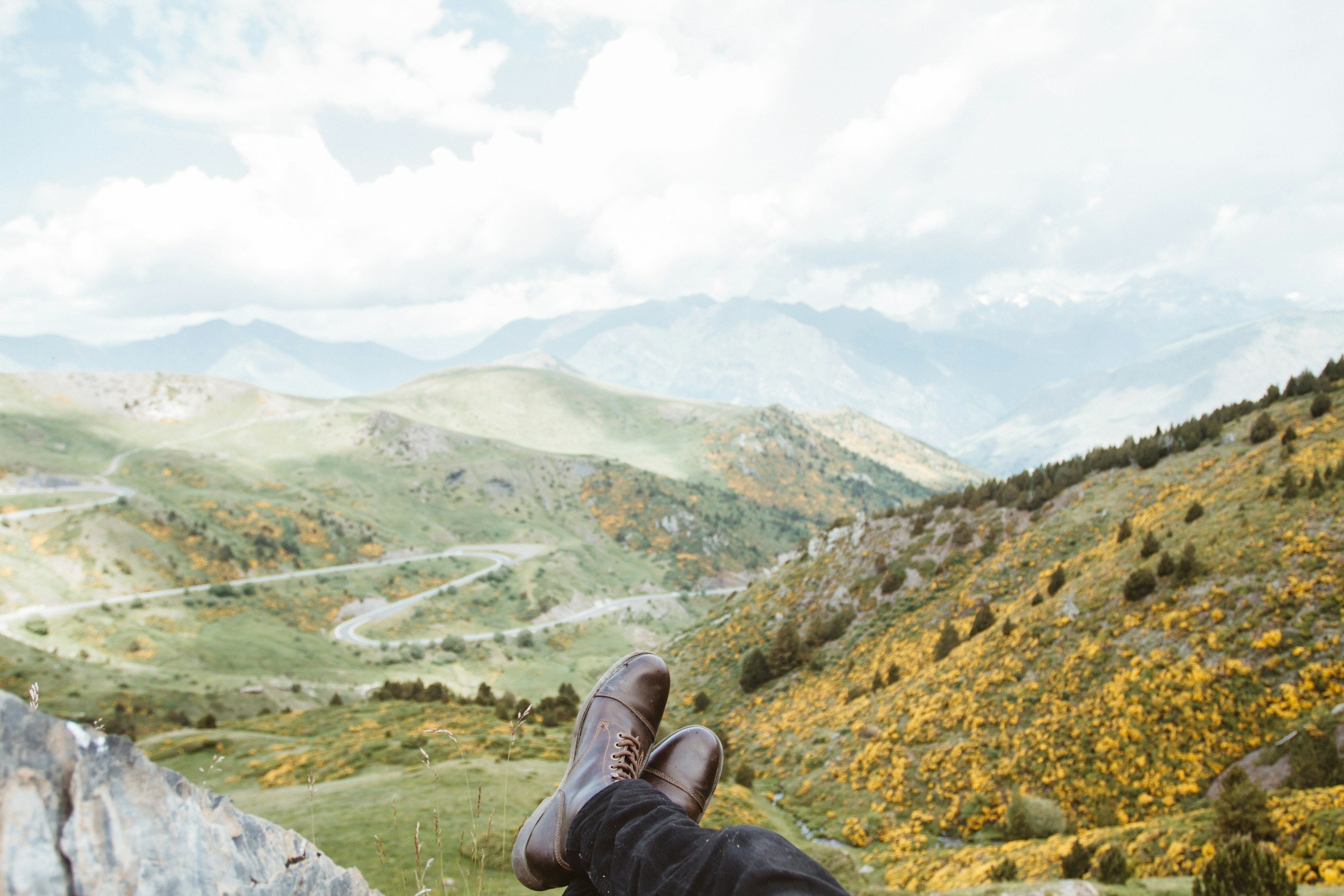 Person relaxing on a rocky ledge overlooking lush mountains and winding roads, representing mindfulness, reflection, and wellbeing at Black Onyx Counselling in London, Ontario