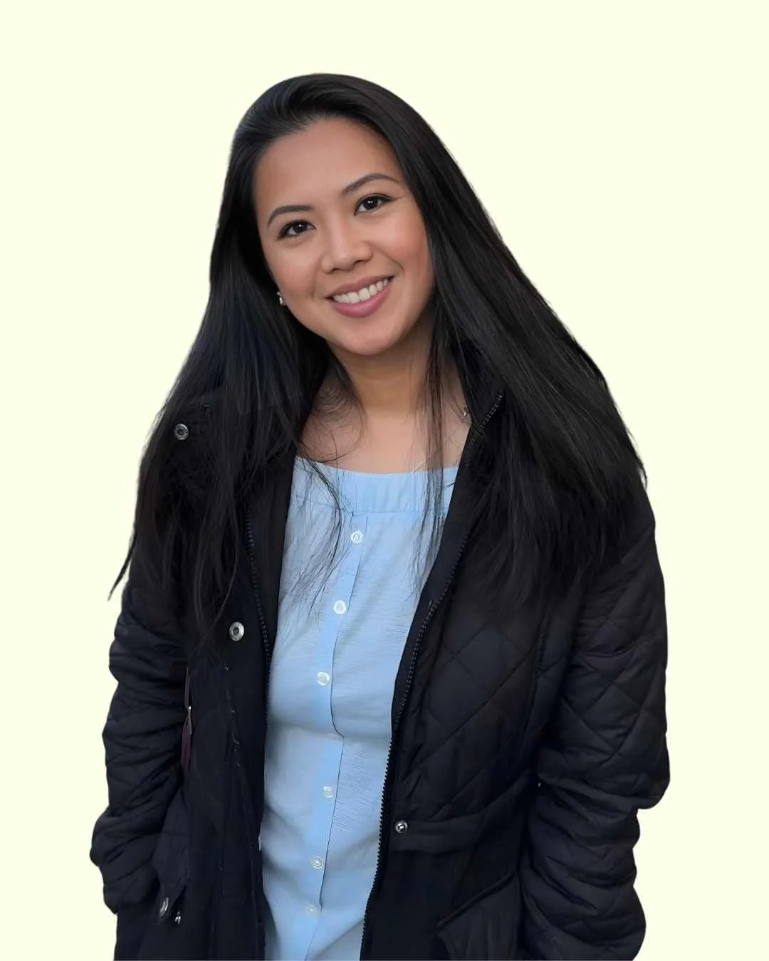 A woman with long black hair smiling, dressed in a light blue button-up shirt and black quilted jacket, against a light-colored background.