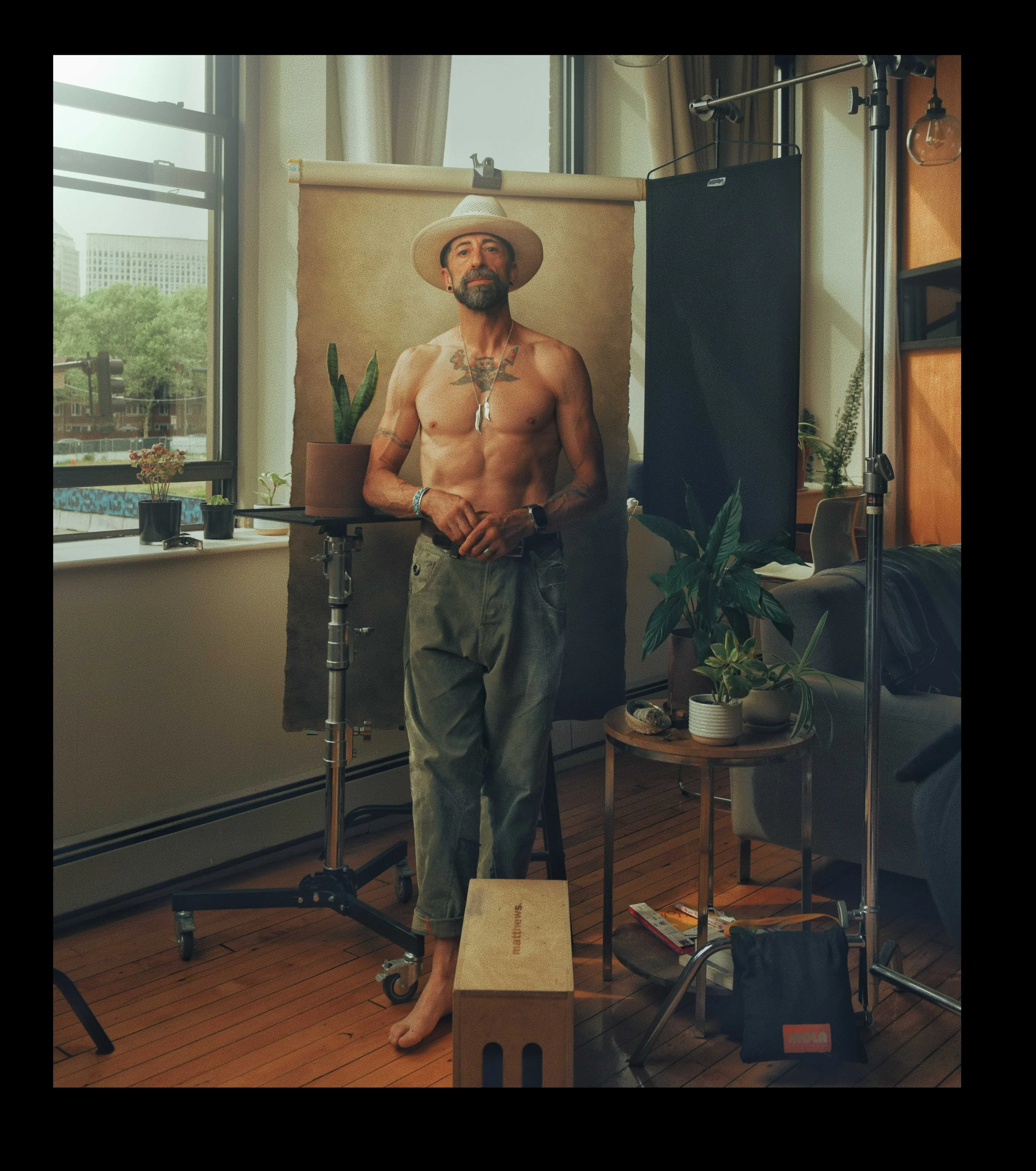 Behind the scenes in the SoWa studio: a tattooed man in a wide brim hat lit against a painted backdrop