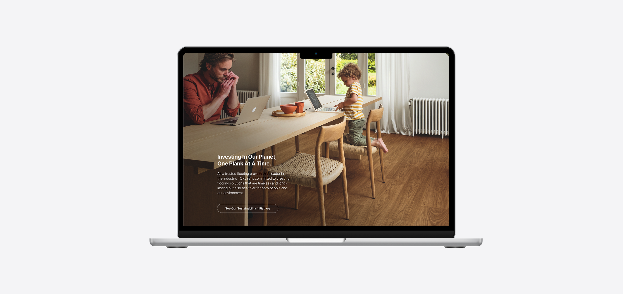 Laptop displaying a webpage with a photo of a man and a child at a kitchen table, the man looks thoughtful and the child is standing on a chair, working on a laptop.
