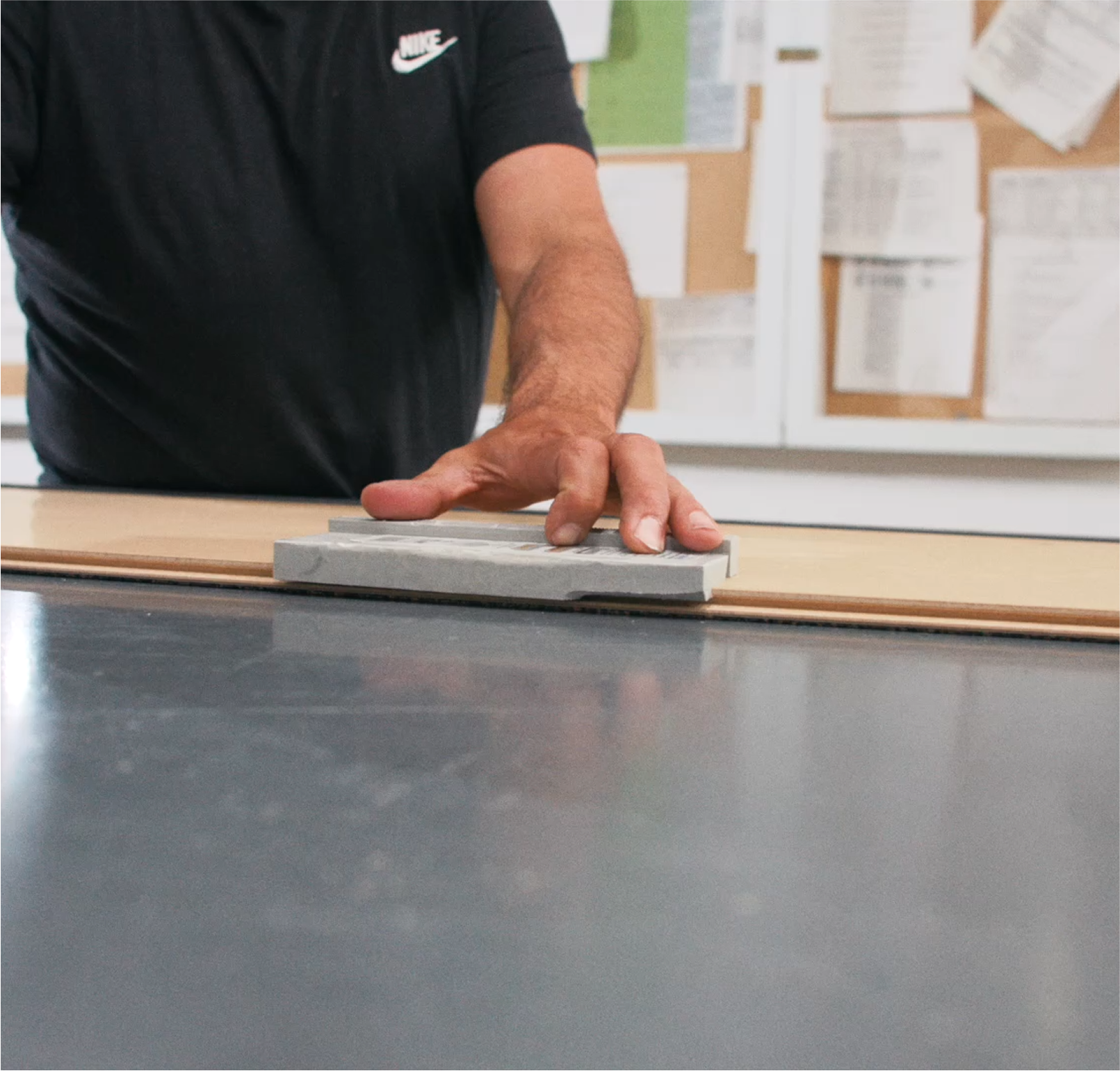 Person wearing a black Nike t-shirt smoothing a surface with a trowel or float in a workshop or construction setting.