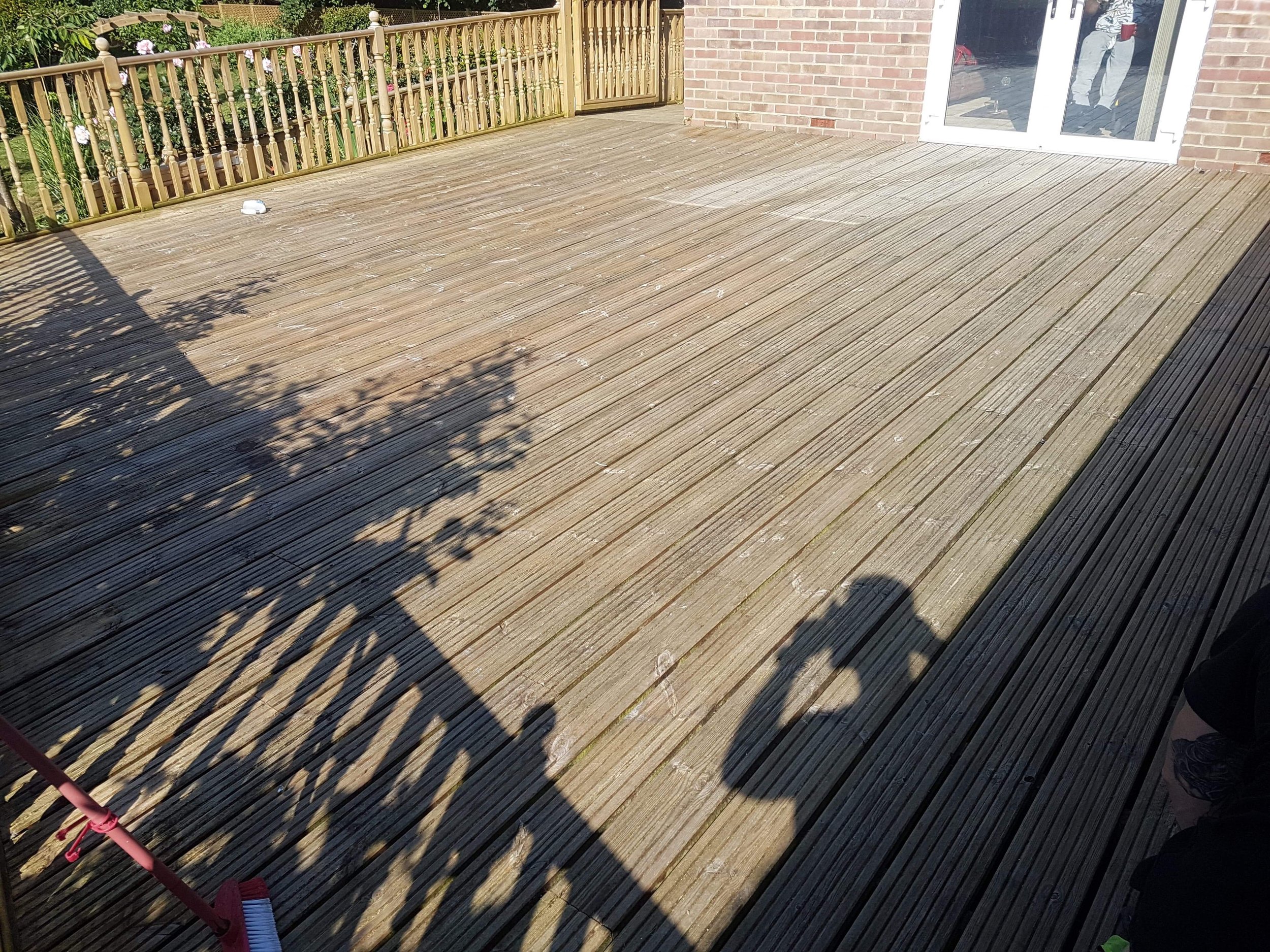 Wooden deck with broom, shadows, garden fence, and sliding glass door