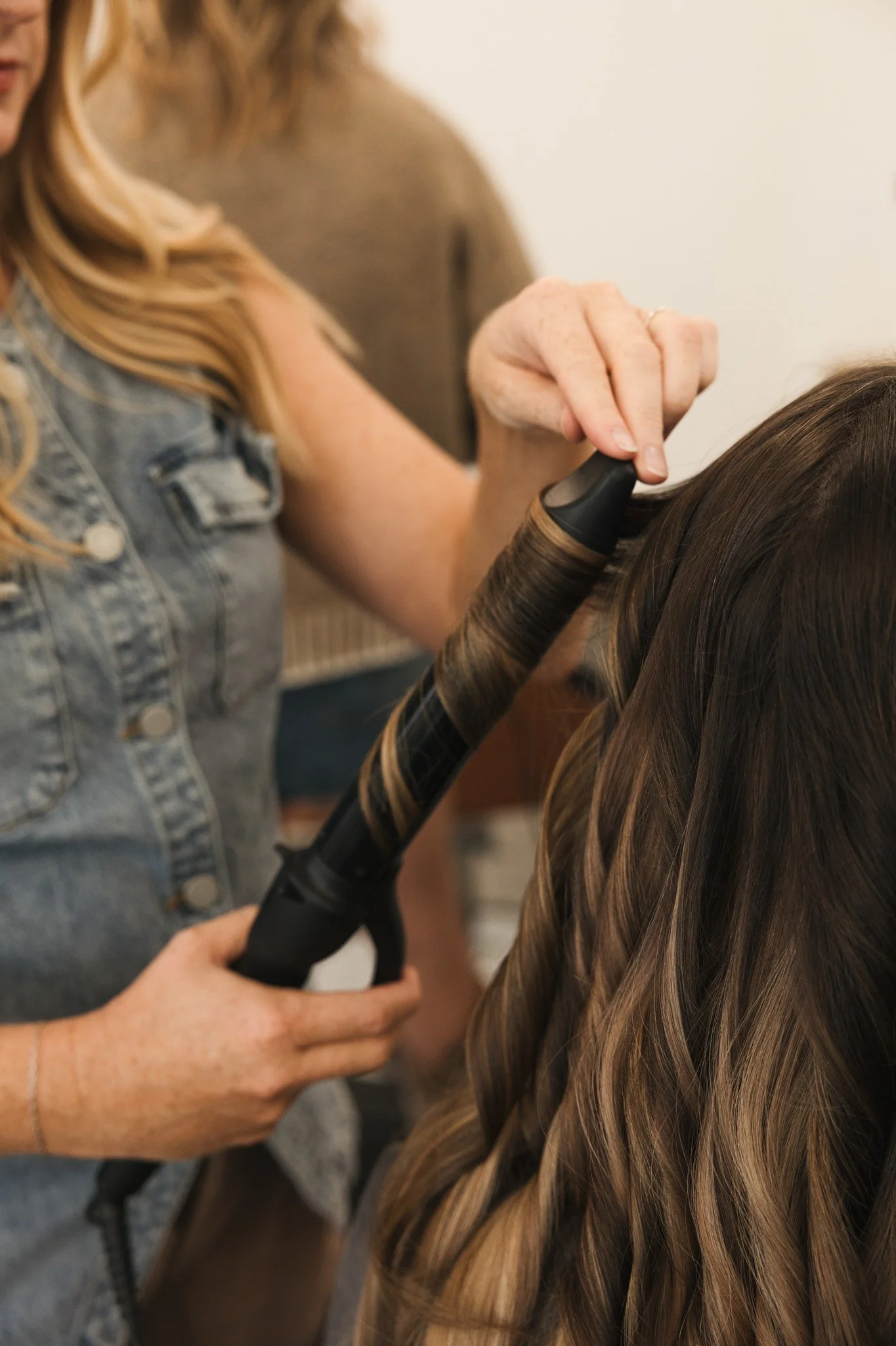 Woman styling long, wavy brown hair with a curling iron in a salon or at home.