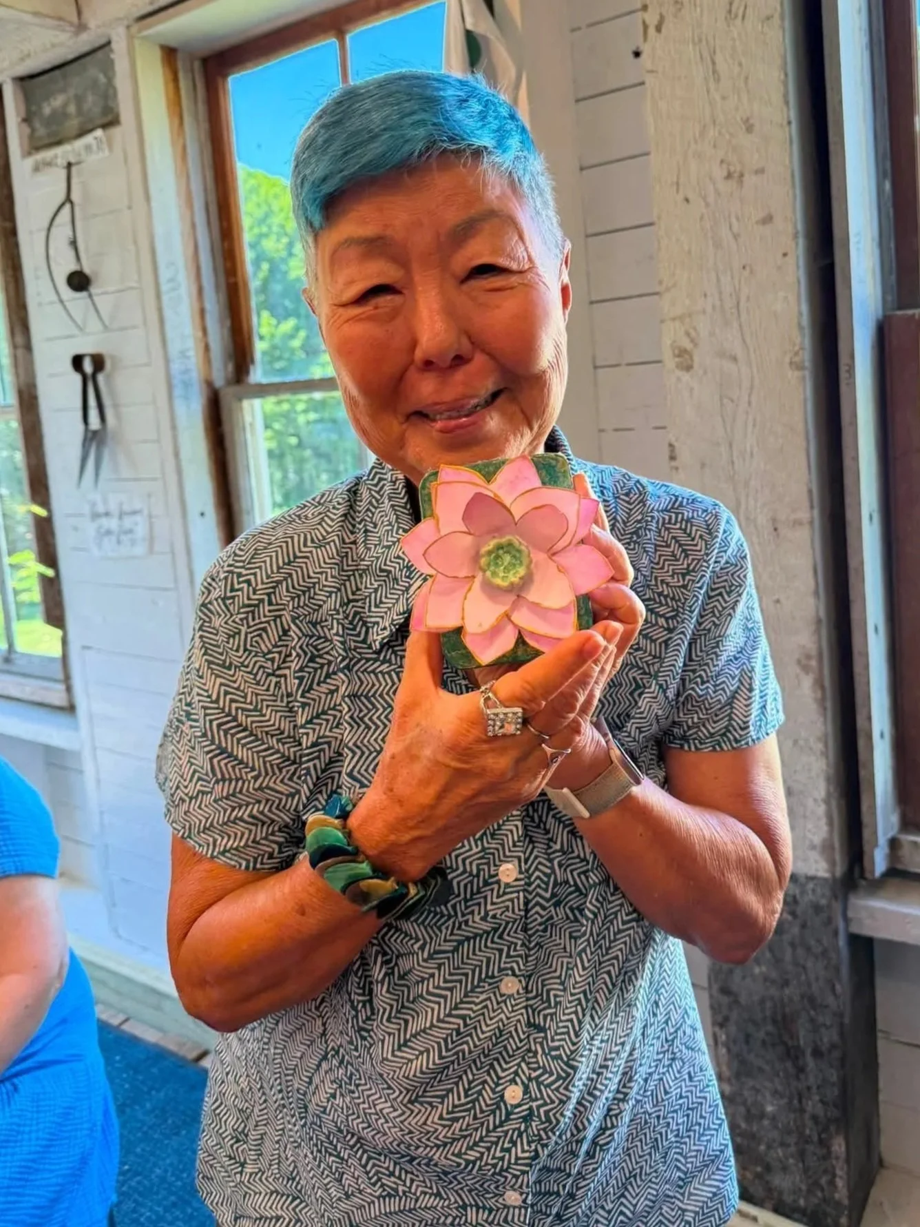 Smiling retreat artist with blue hair holding a pink handmade paper flower in the barn studio