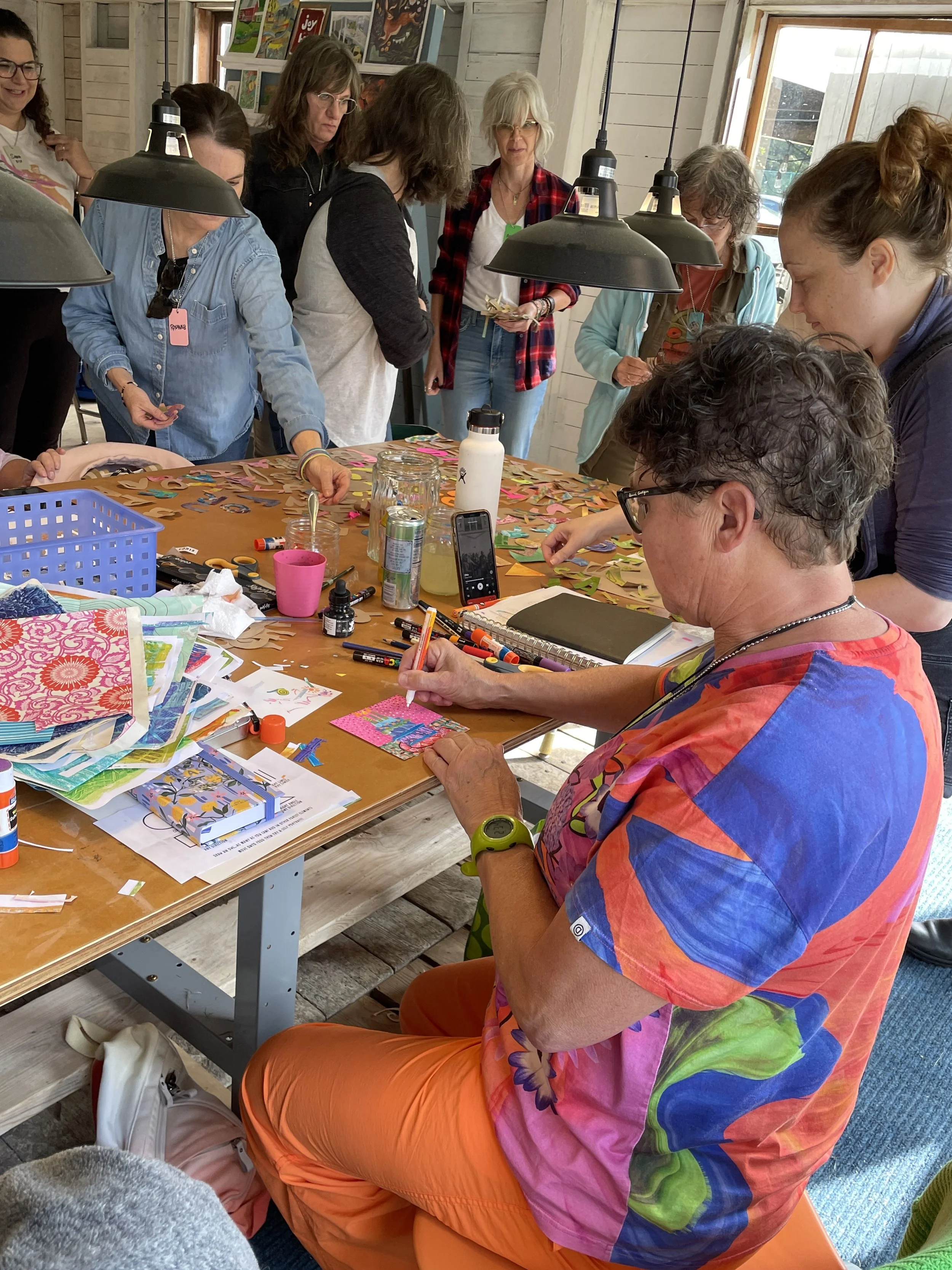 Artists gathered around a busy collage table, cutting and gluing paper in the barn studio