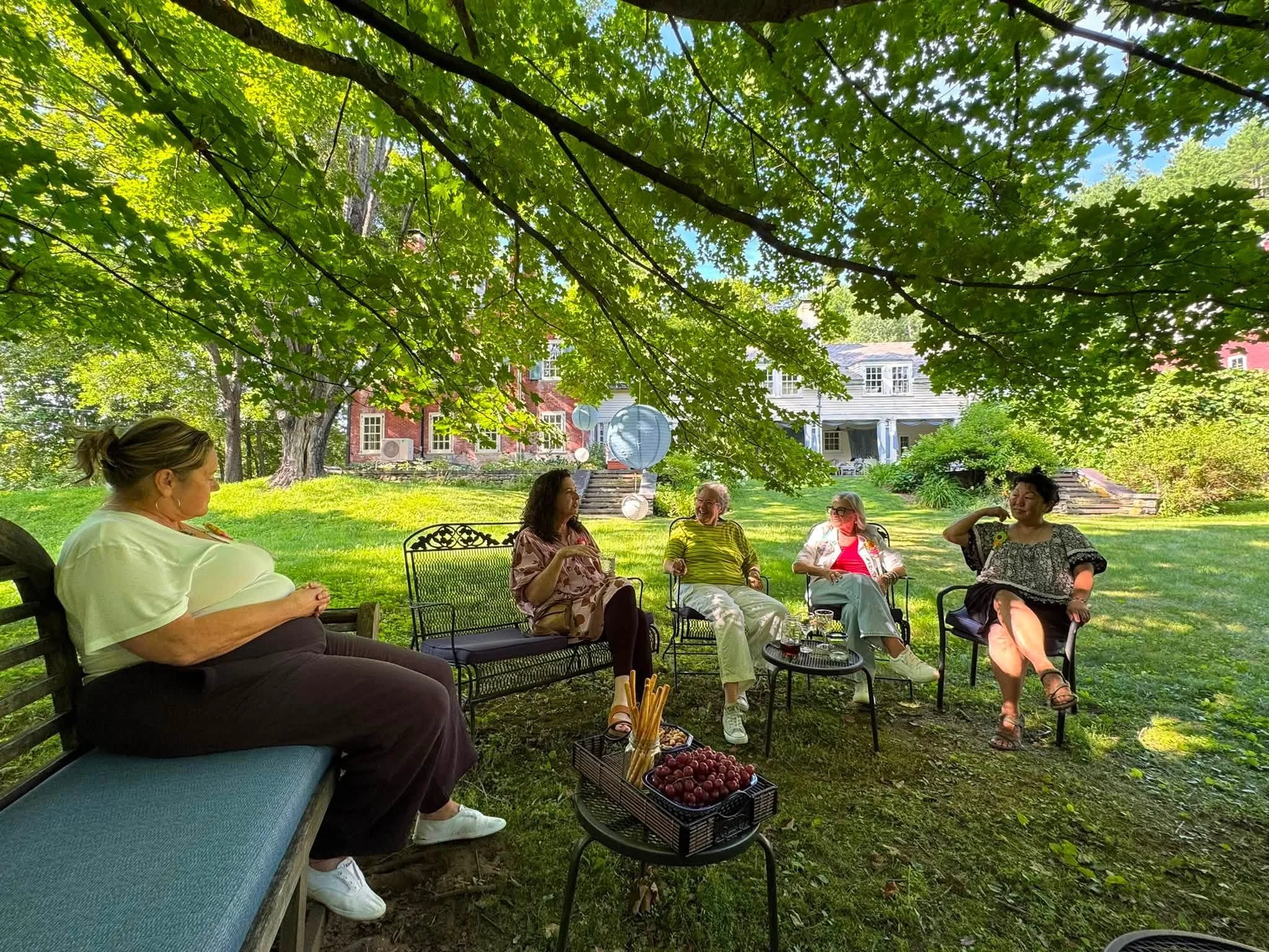 Retreat artists relaxing in lawn chairs in the shade of a maple tree with The Smiley Manse behind them