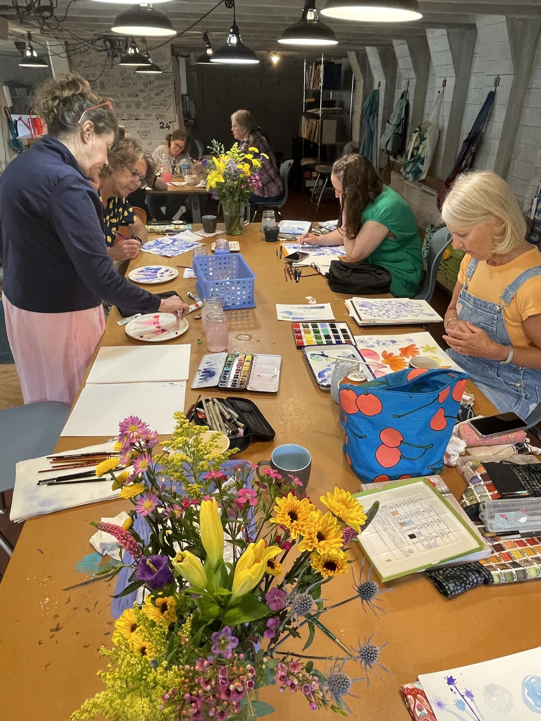 Artists painting with watercolors at a long table with a bouquet of flowers in the barn studio