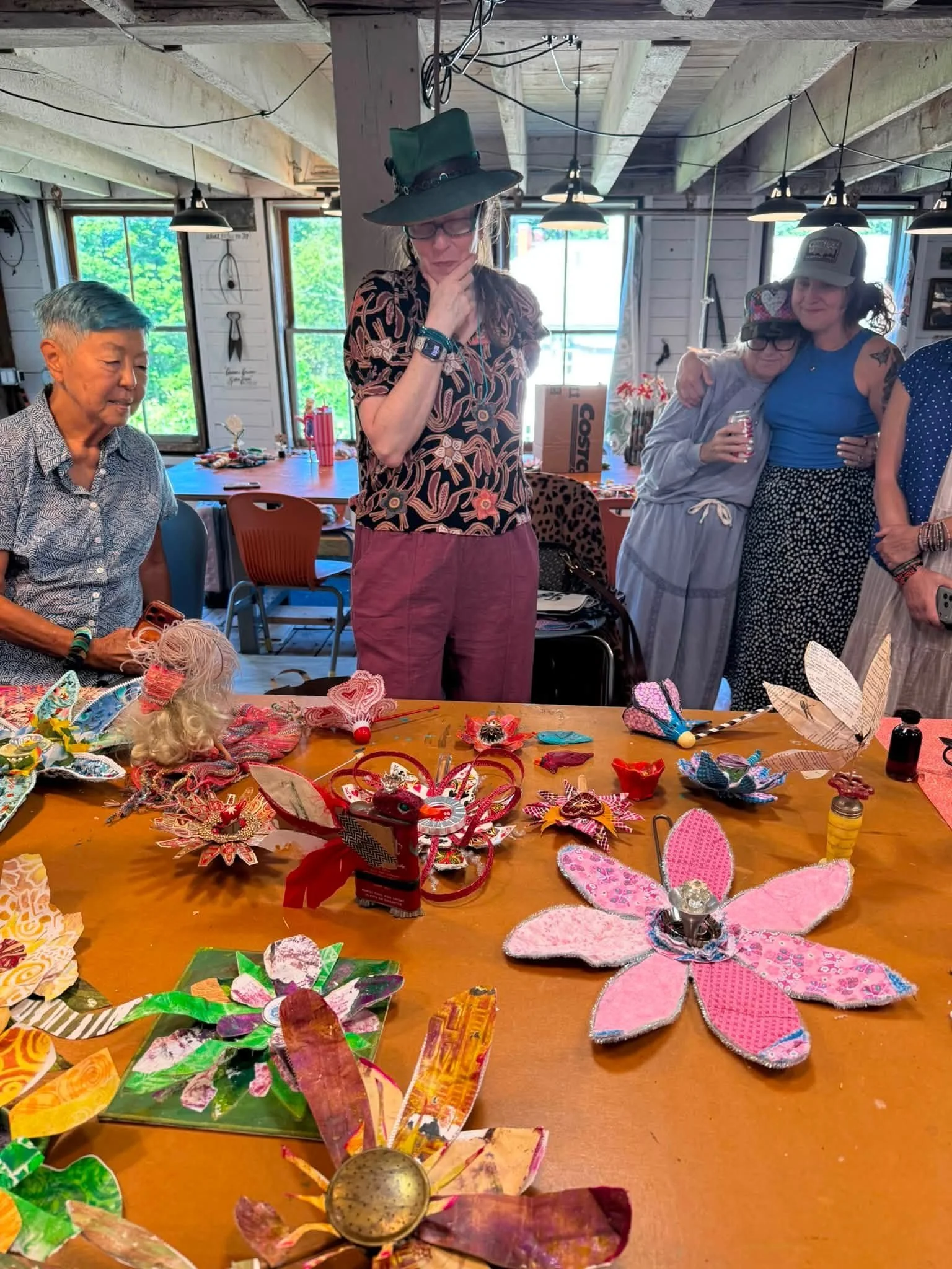 Retreat artists gathered around a studio table covered with handmade paper and metal flowers in the Smiley Manse barn