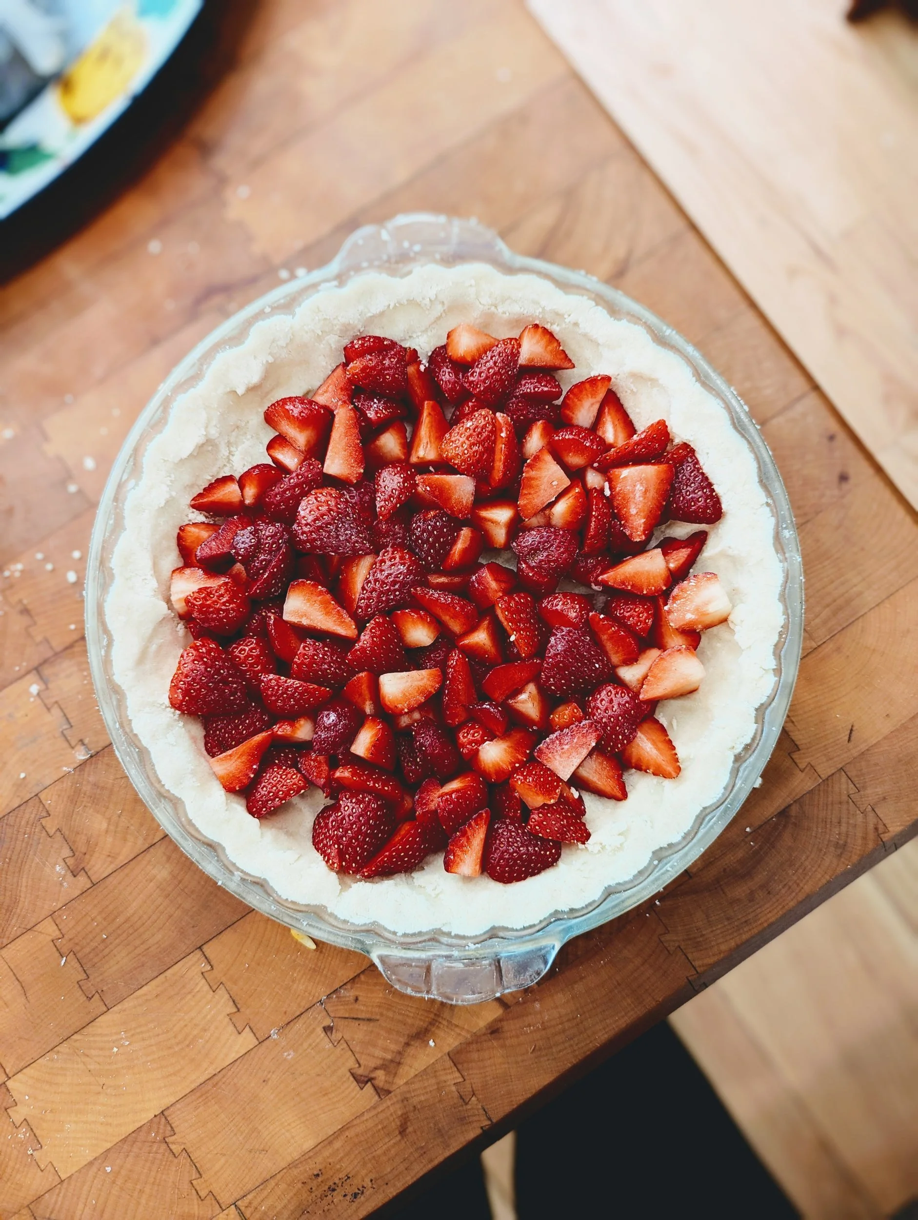 Round tart topped with sliced fresh strawberries on a glass cake stand on a butcher block counter