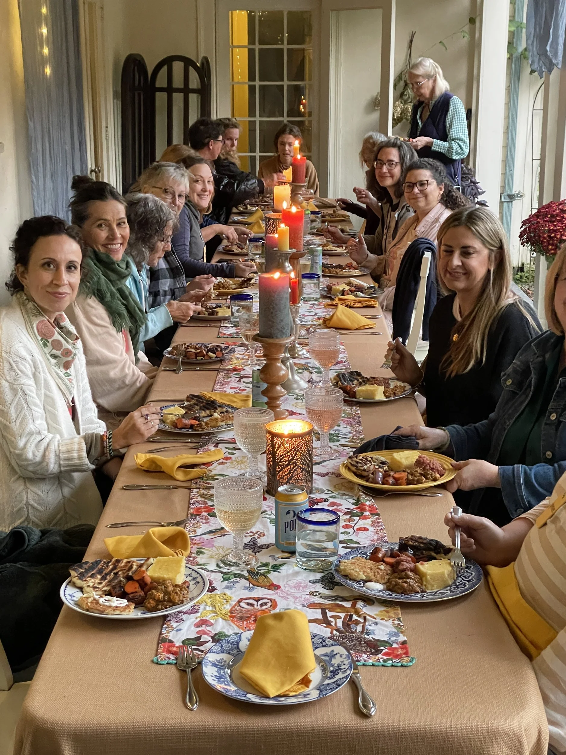 Retreat artists seated along a long candlelit porch table set for dinner in early autumn