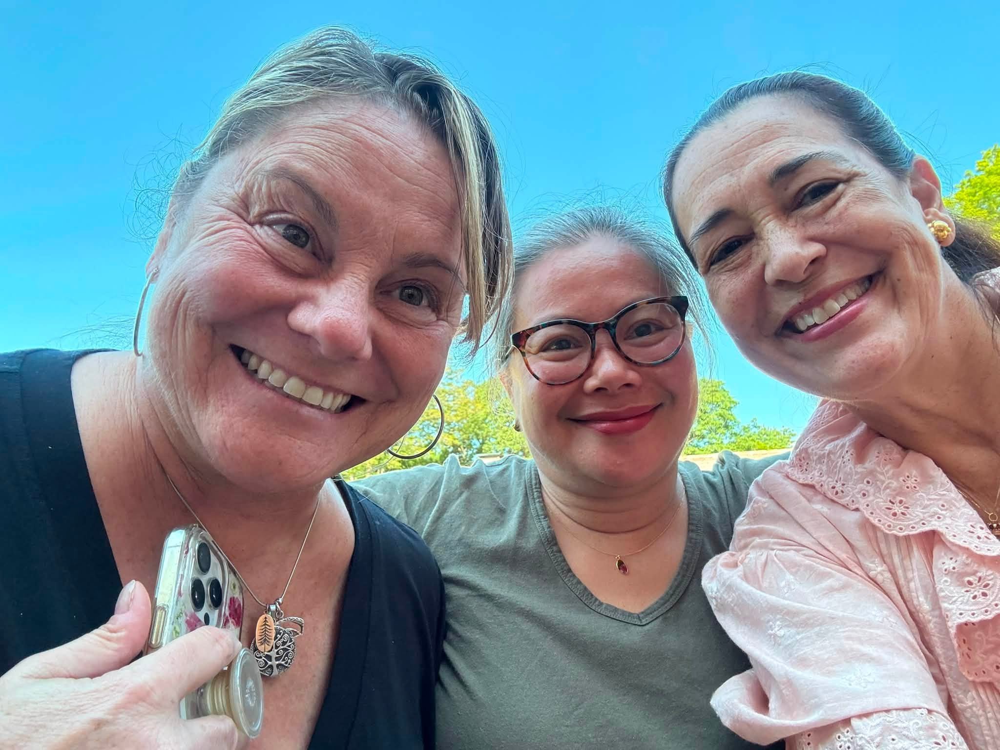 Three smiling retreat artists leaning together for an outdoor selfie under a blue sky