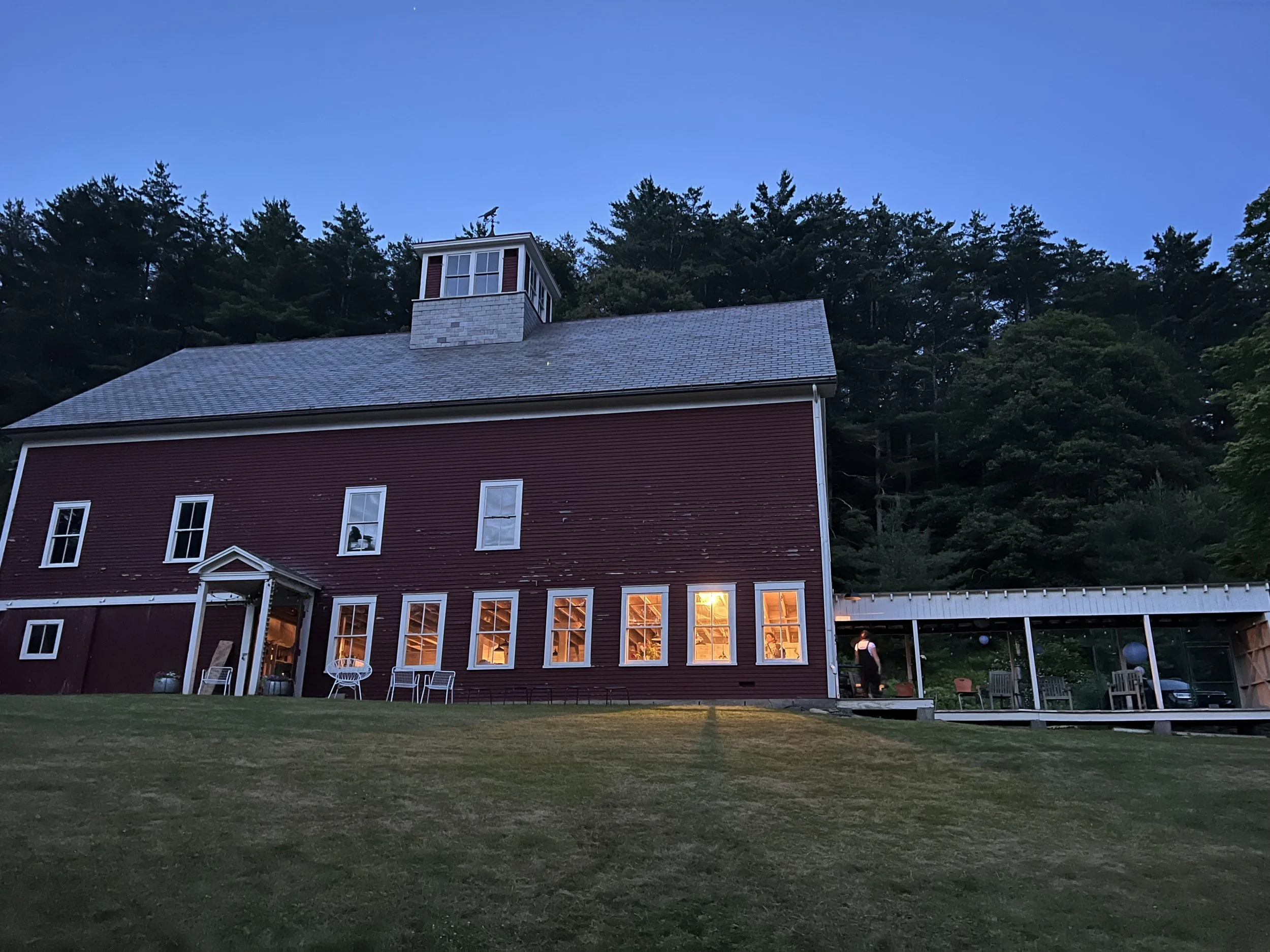 Red barn studio with lit windows at dusk under a deep blue sky above a dark lawn