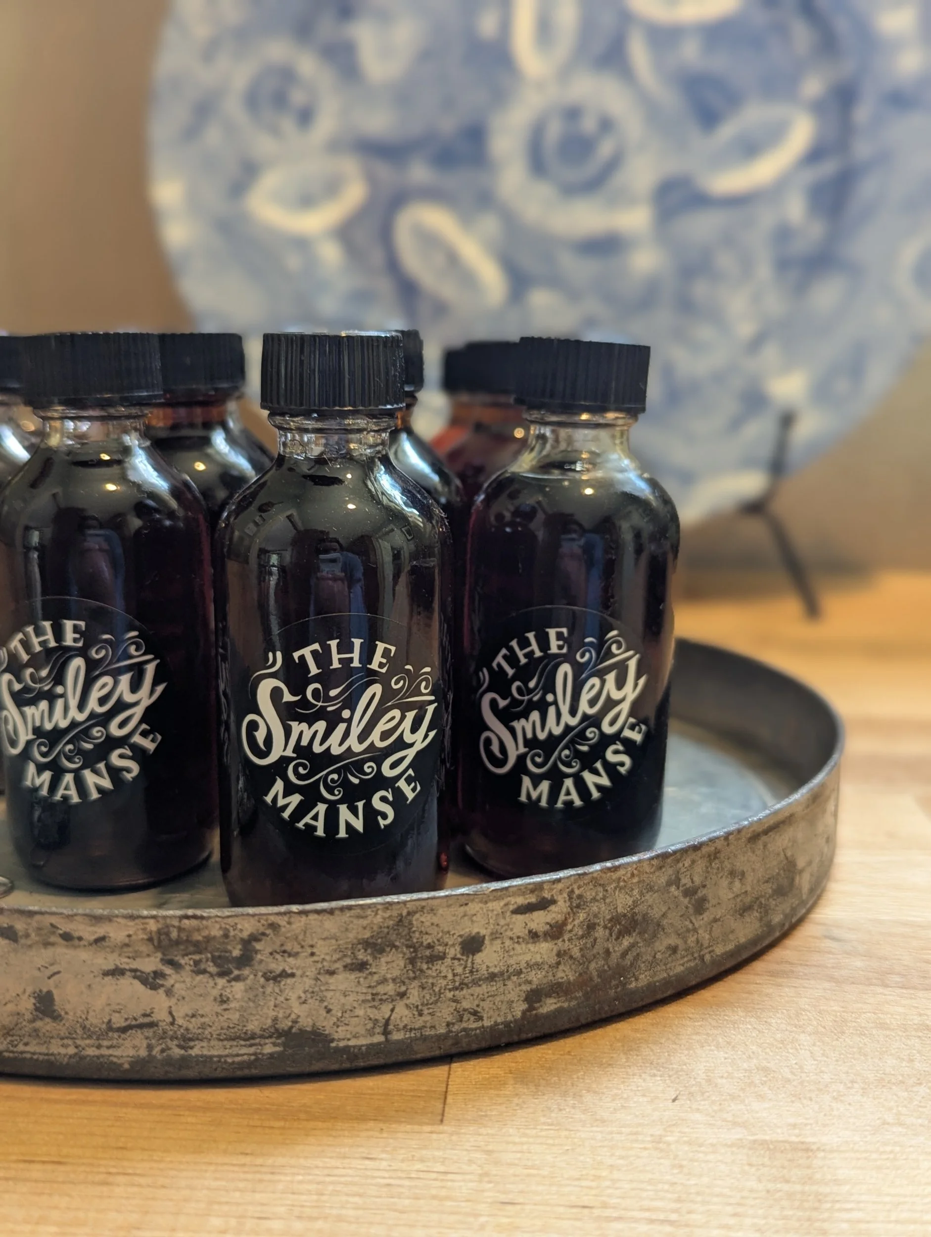 Dark glass bottles of homemade syrup with The Smiley Manse labels on a vintage metal tray