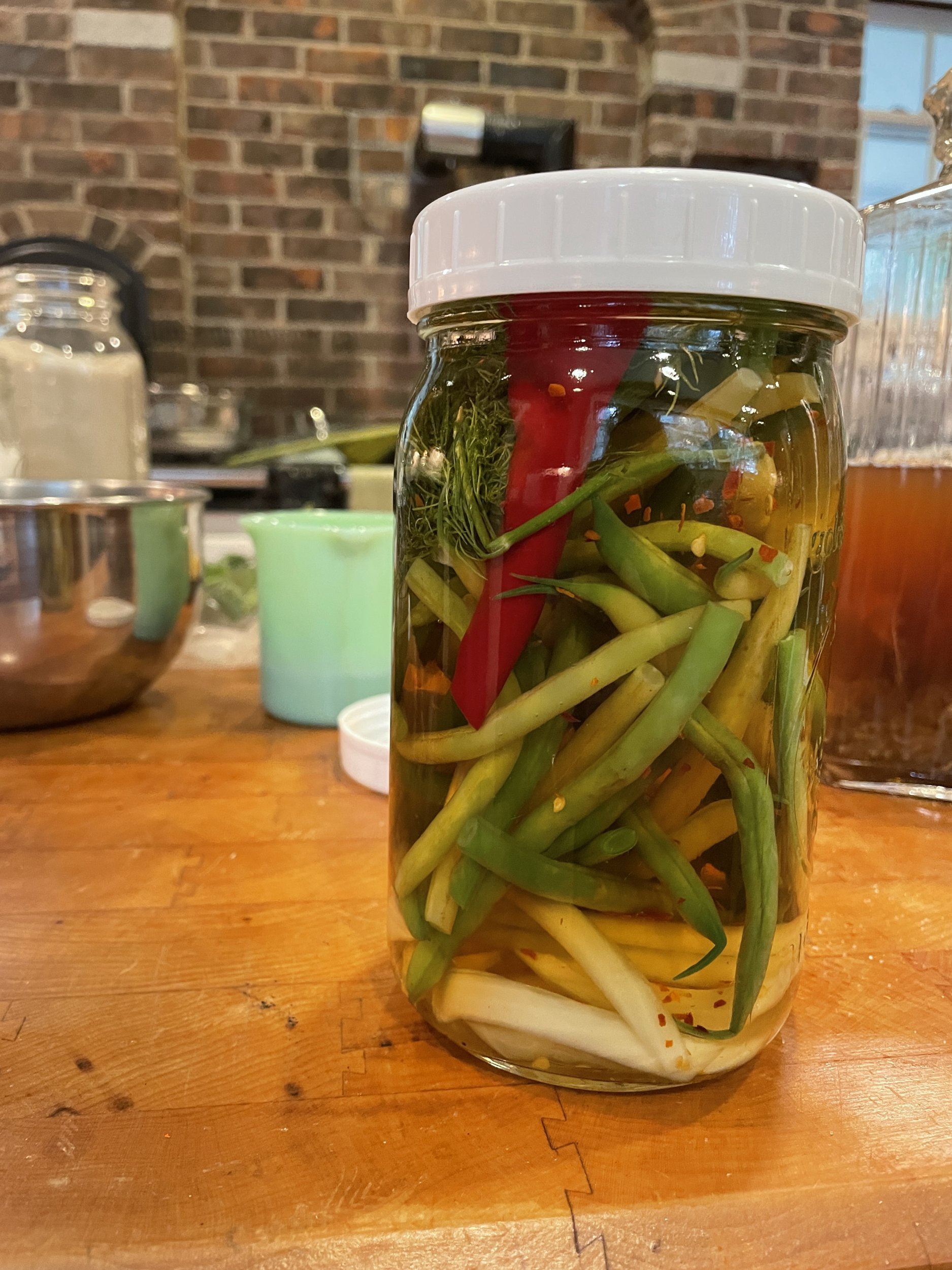 Jar of pickled green and yellow beans with a red pepper on a wooden butcher block counter