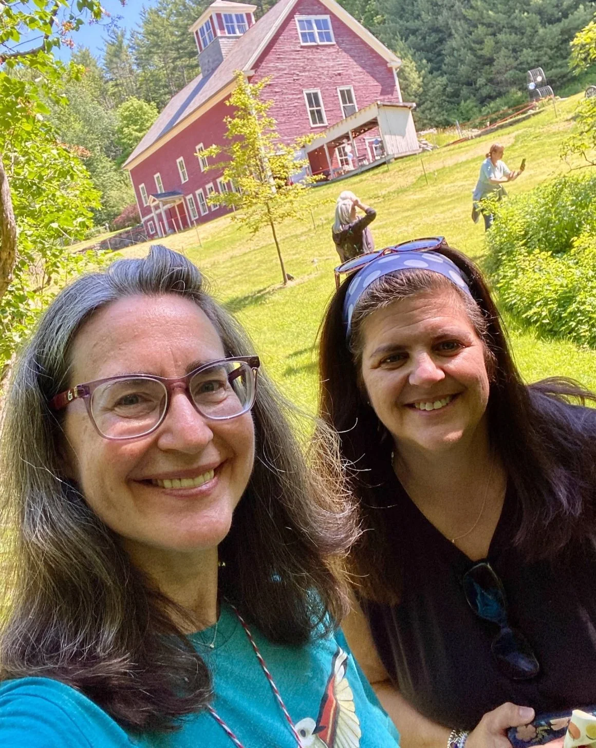 Two smiling retreat artists taking a selfie on the sunny hillside with the red barn behind them.