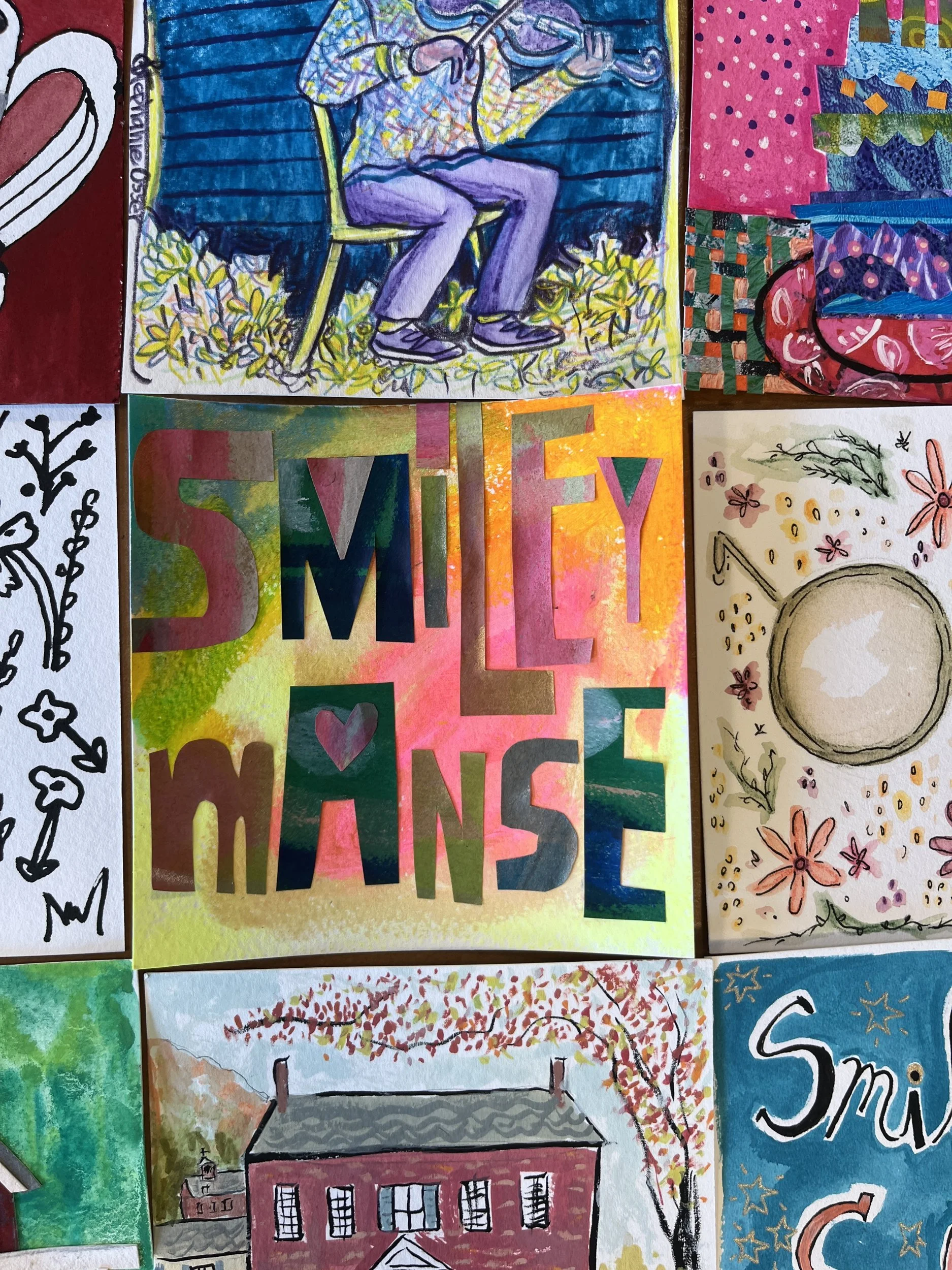 Wall of colorful art cards featuring Smiley Manse lettering, a fiddler and the brick manse