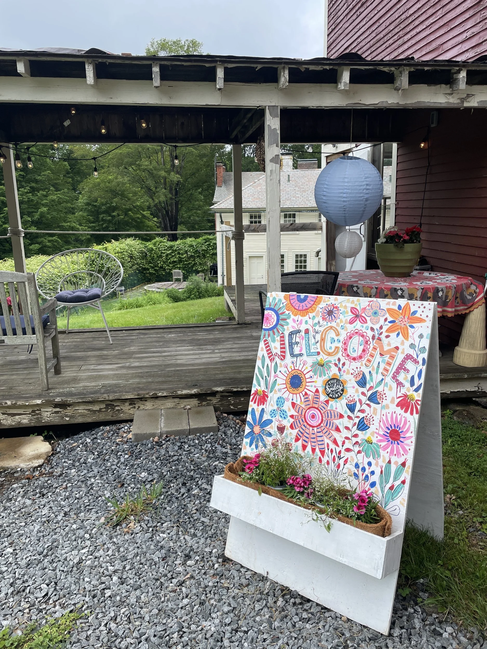 Hand-painted floral welcome sign on the barn porch with paper lanterns and the lawn beyond