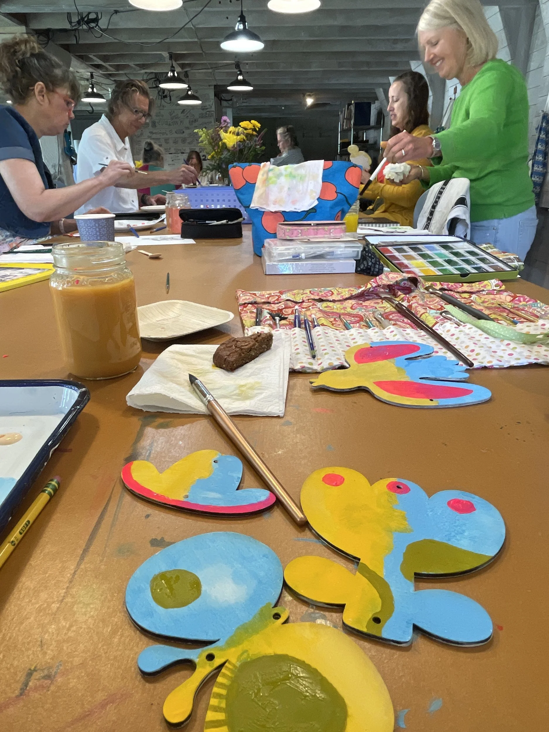 Painted wooden butterflies in blue, yellow and pink on the studio table with artists working in the background
